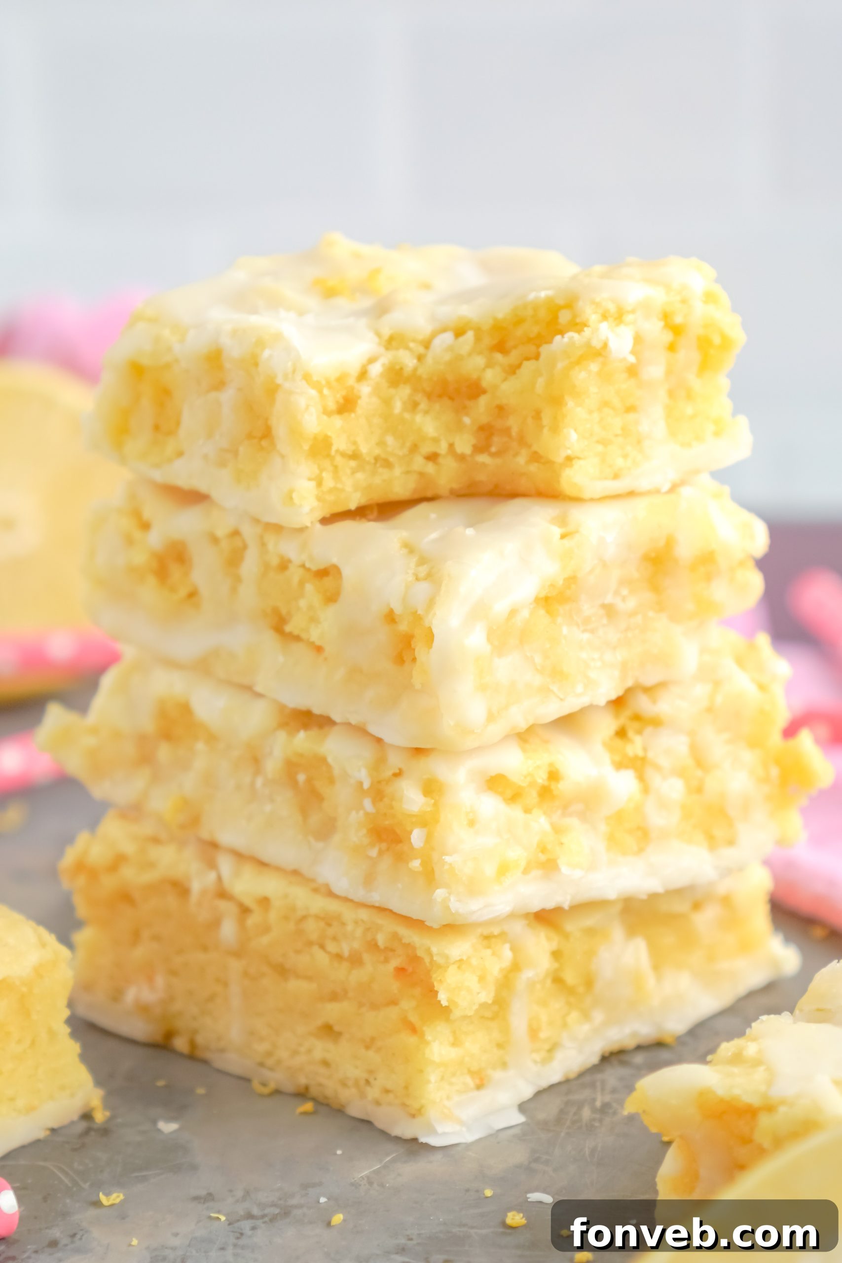 Moist lemon brownies topped with a generous amount of tangy lemon glaze, sliced and ready to serve on a white surface.