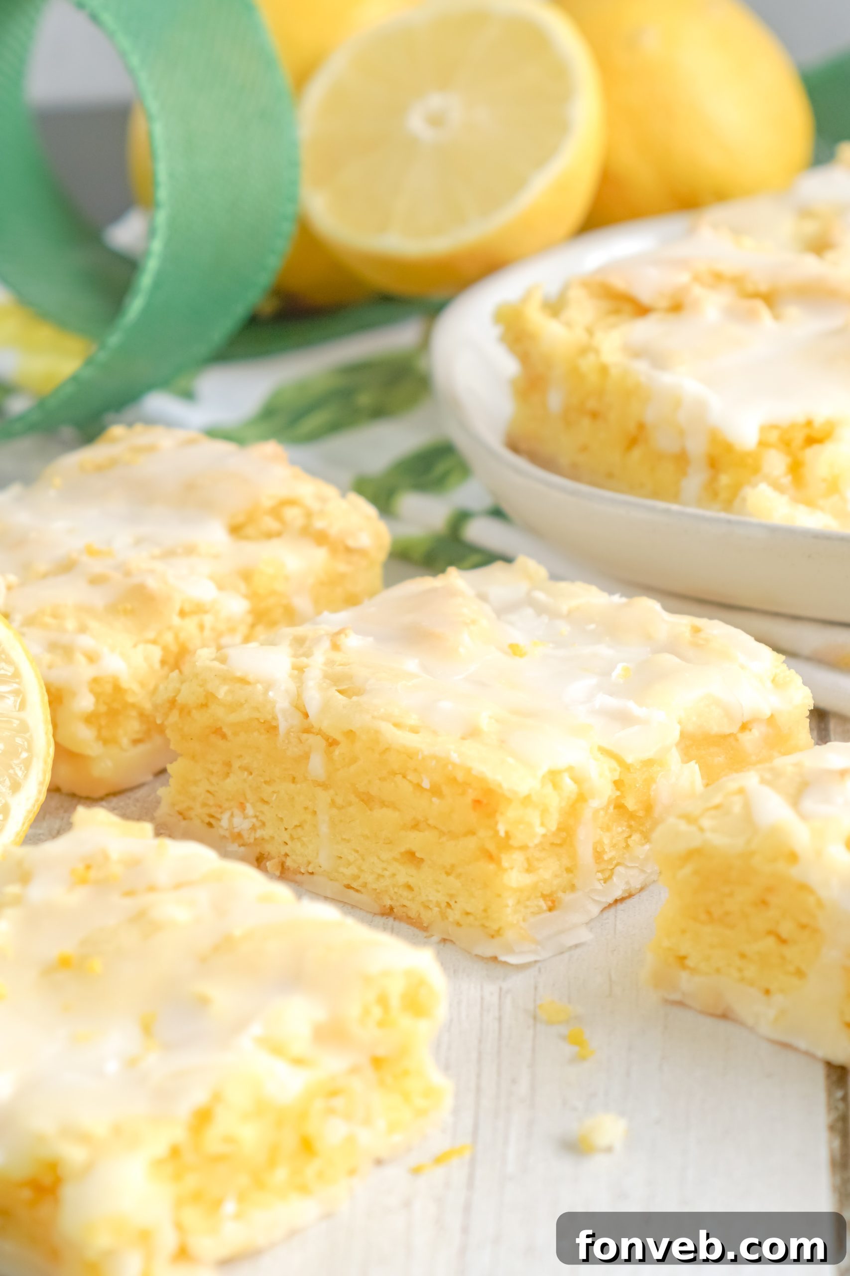 A stack of four glazed lemon brownies, artfully arranged and garnished with delicate strands of lemon zest.