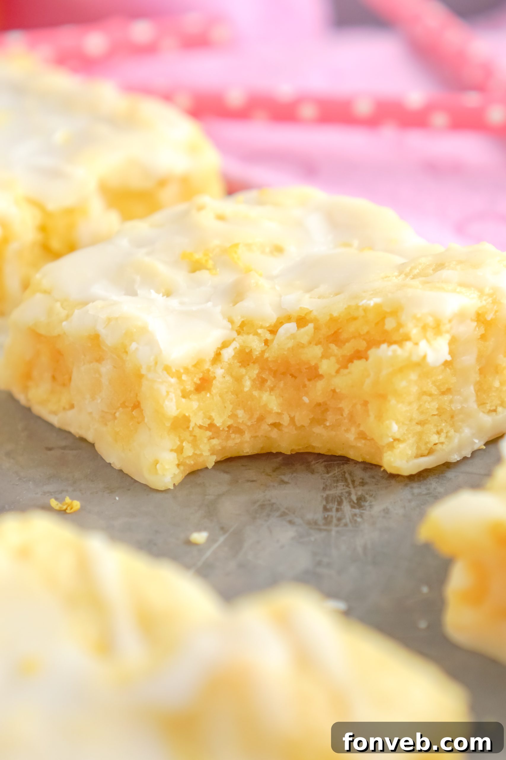 A rustic bowl filled with fresh, bright yellow lemons, with a stack of glazed lemon brownies blurred in the background.
