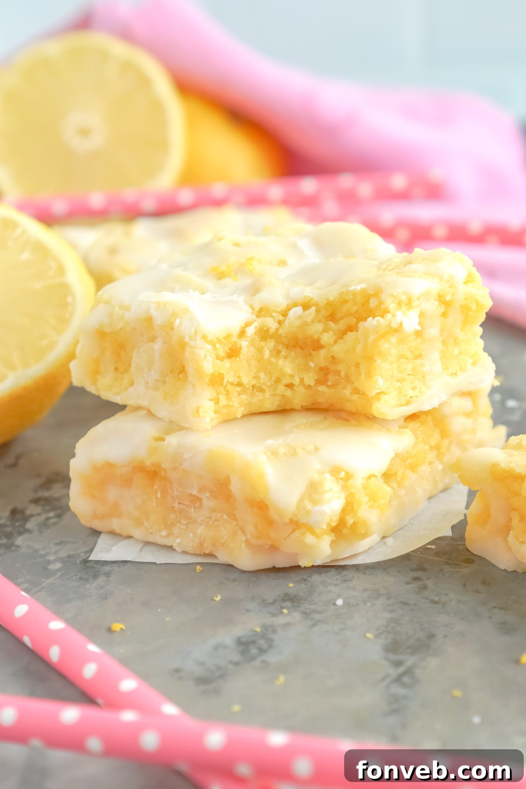Two glazed lemon brownies garnished with fresh lemon slices, presented on a minimalist white plate.