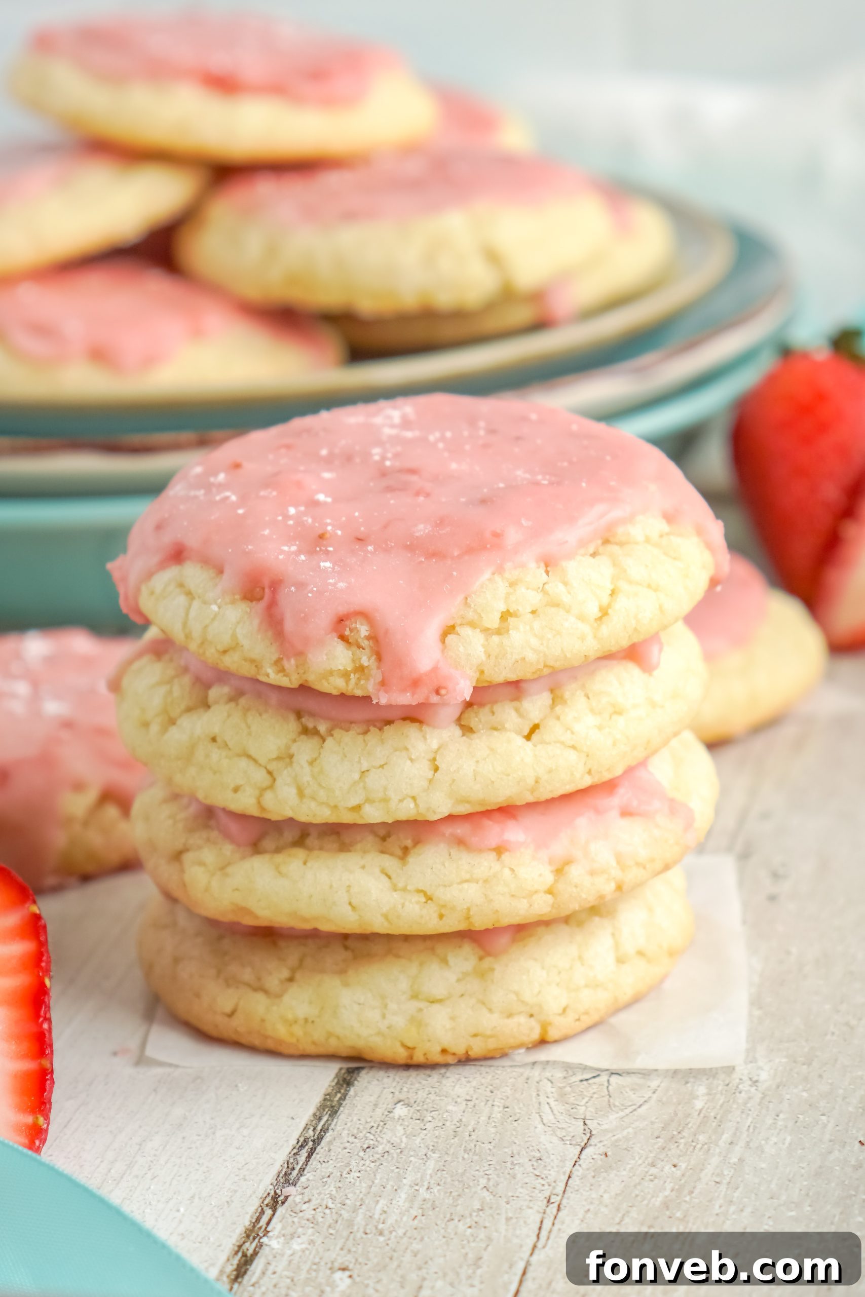 A stack of strawberry glazed sugar cookies separated by parchment paper in a storage container, demonstrating proper storage.