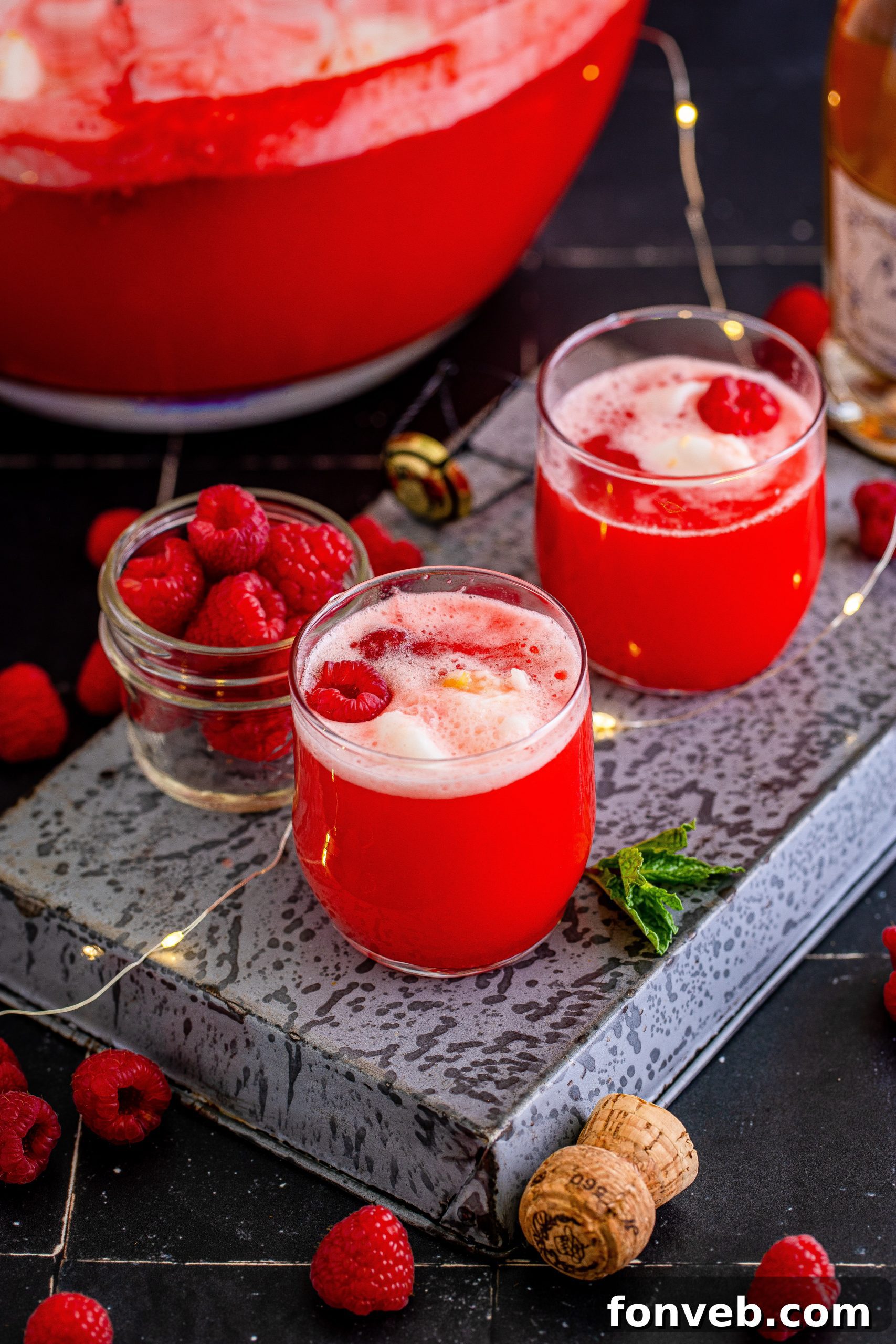 Hands stirring the Boozy Sherbet Punch in a large punch bowl, preparing it for serving.