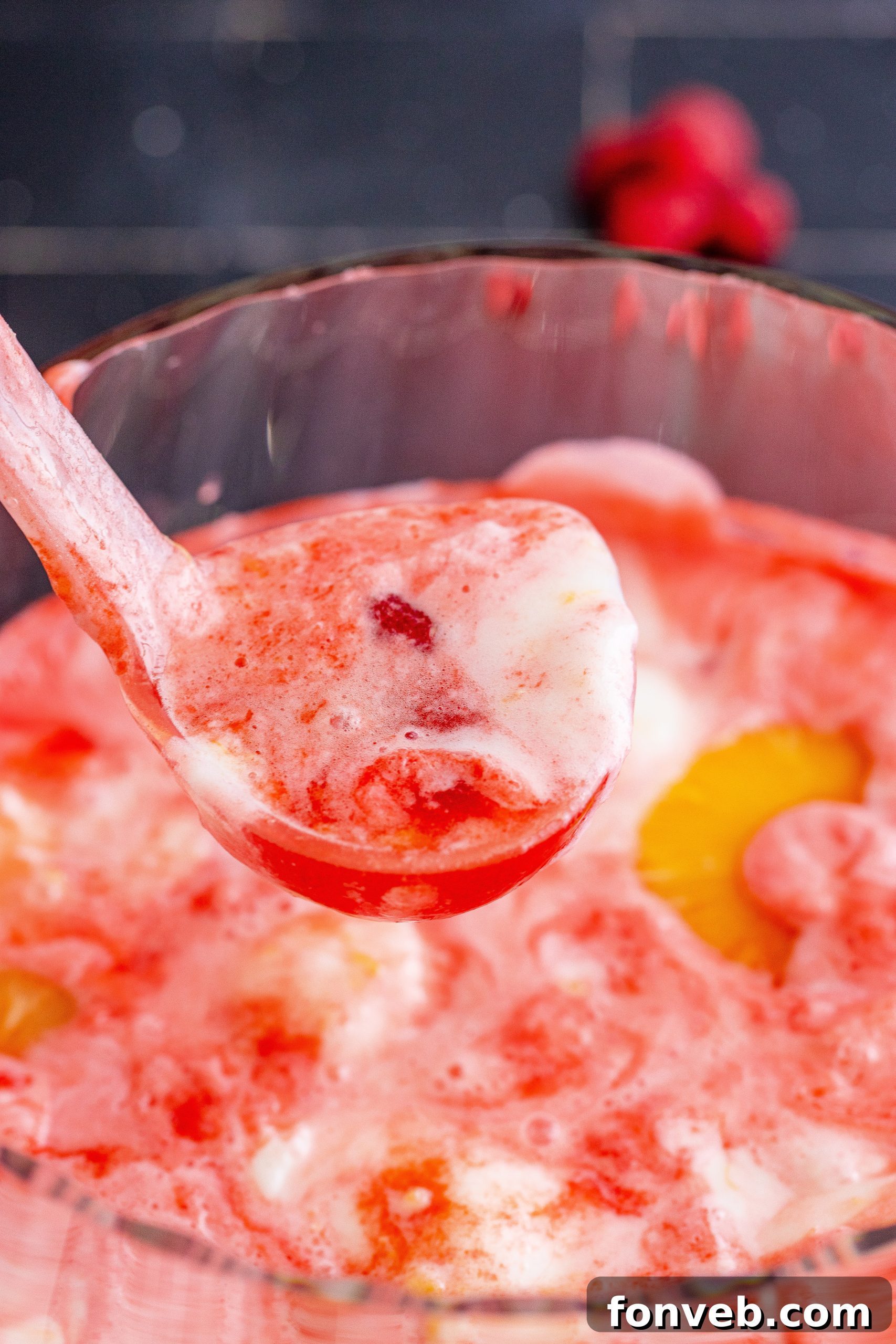 Close-up of a glass of boozy sherbet punch garnished with fresh raspberries and a mini pineapple slice.