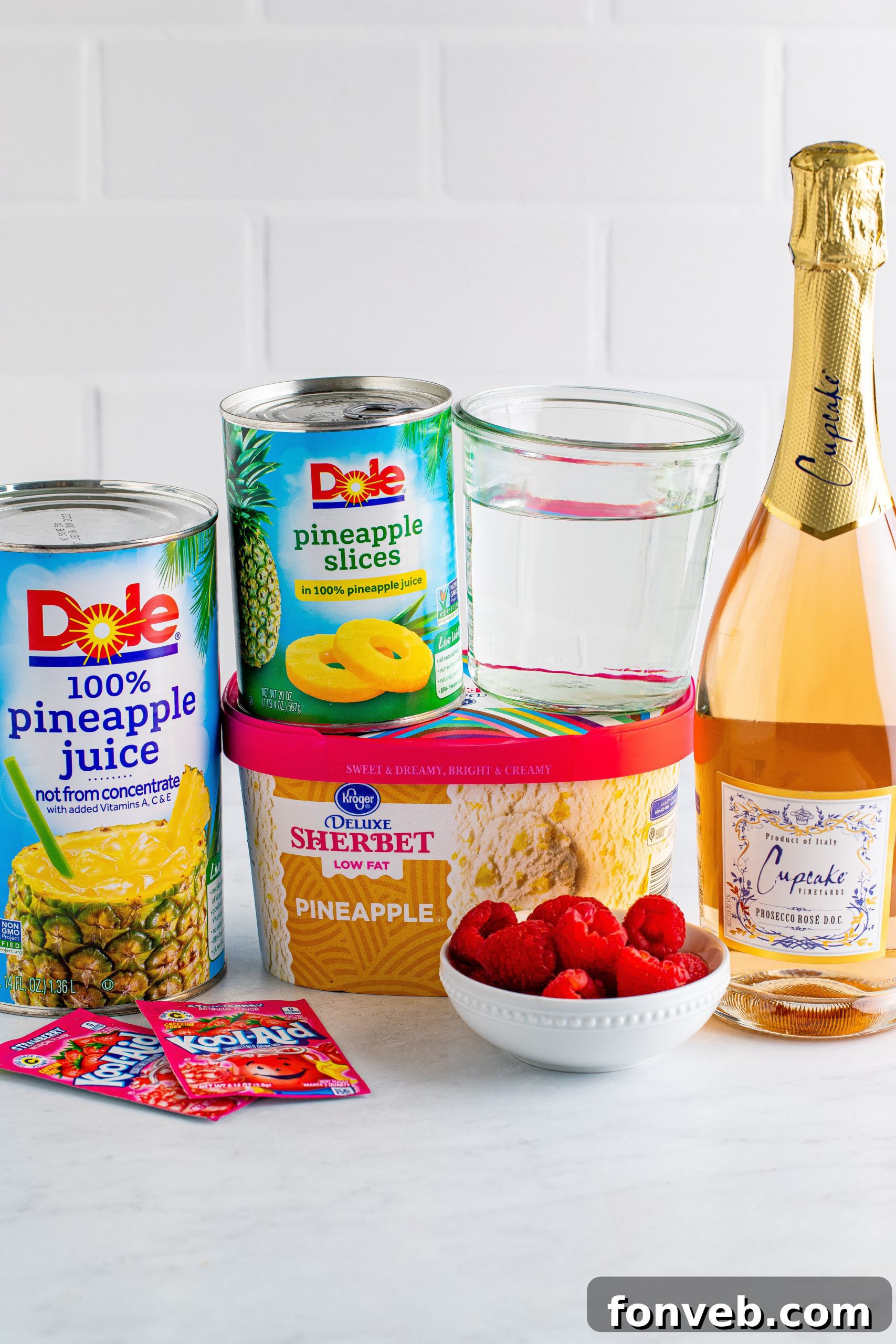 Ingredients for boozy sherbet punch laid out: prosecco bottle, pineapple juice, and strawberry drink mix.