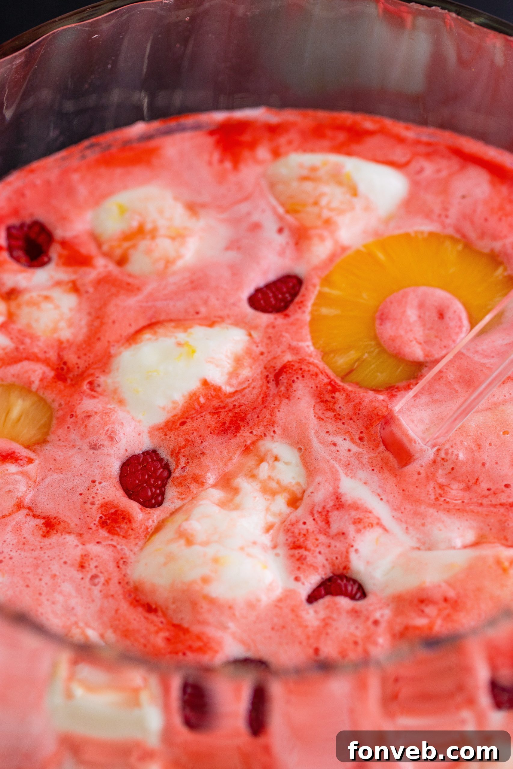 A glass of boozy sherbet punch with a raspberry and a small scoop of sherbet floating on top.