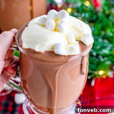 A close-up of a steaming mug of luscious slow cooker hot chocolate, topped with a generous swirl of whipped cream and delicate chocolate shavings, inviting a warm sip.