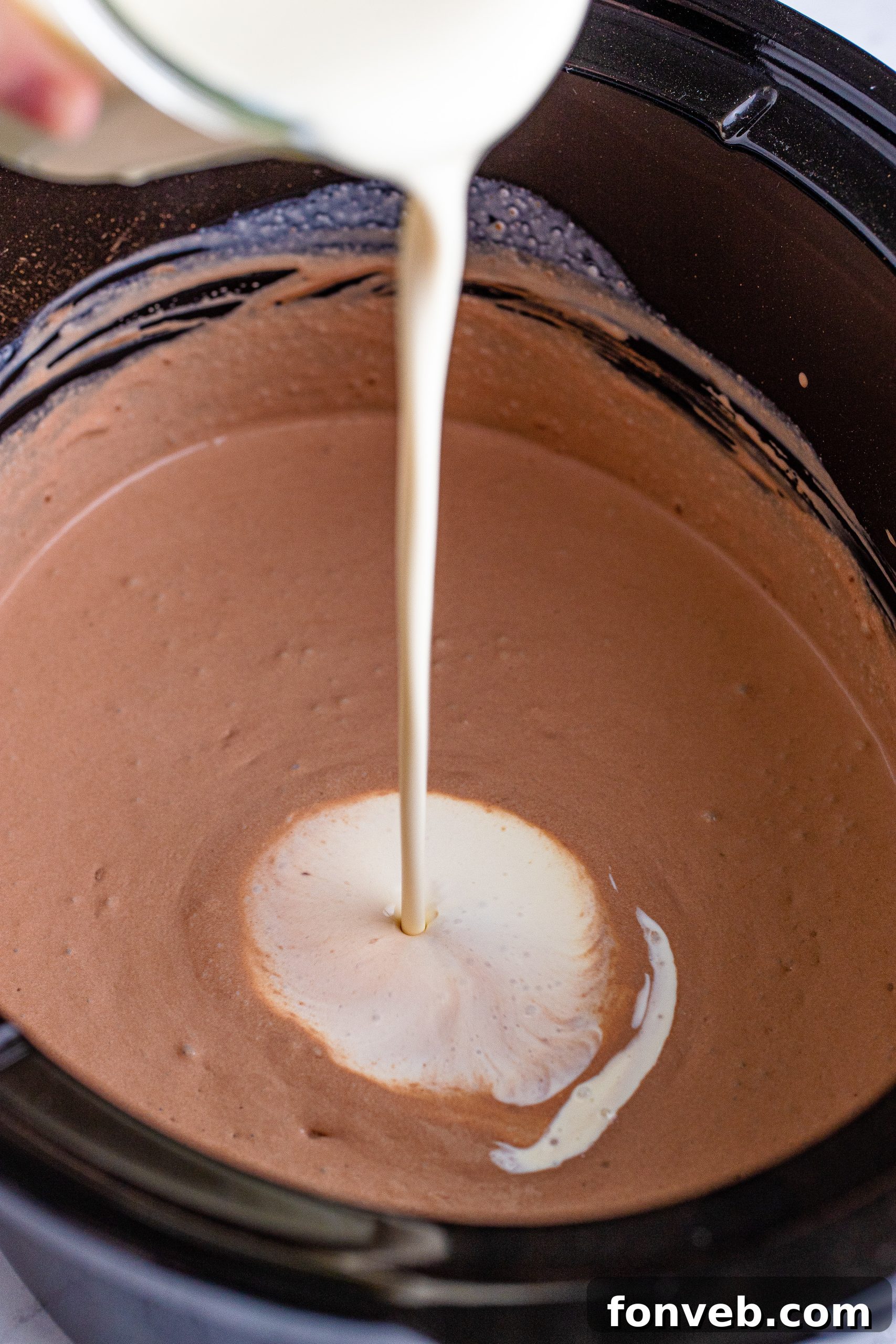 Hands stirring the rich, dark hot chocolate in a slow cooker with a whisk, ensuring all ingredients are well combined and melted.