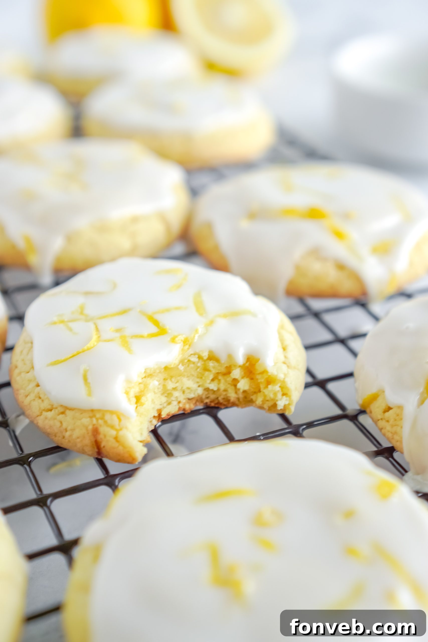 A close-up of a single lemon cake mix cookie adorned with a thick, glossy lemon glaze and a delicate sprinkle of fresh lemon zest, ready to be enjoyed.