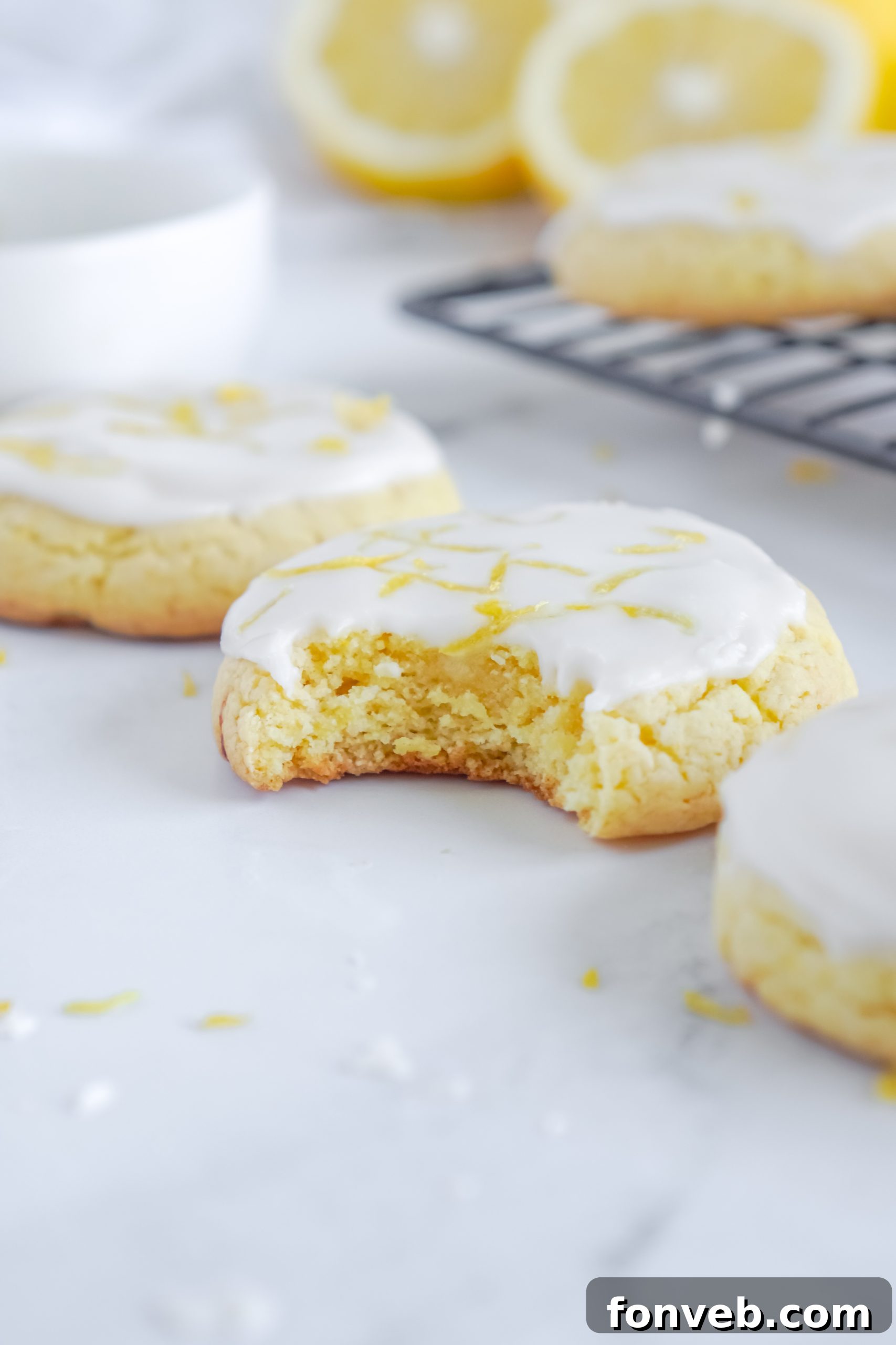 A perfectly arranged stack of lemon cake mix cookies, gleaming with glaze, on a wire cooling rack, with more cookies visible in the background.
