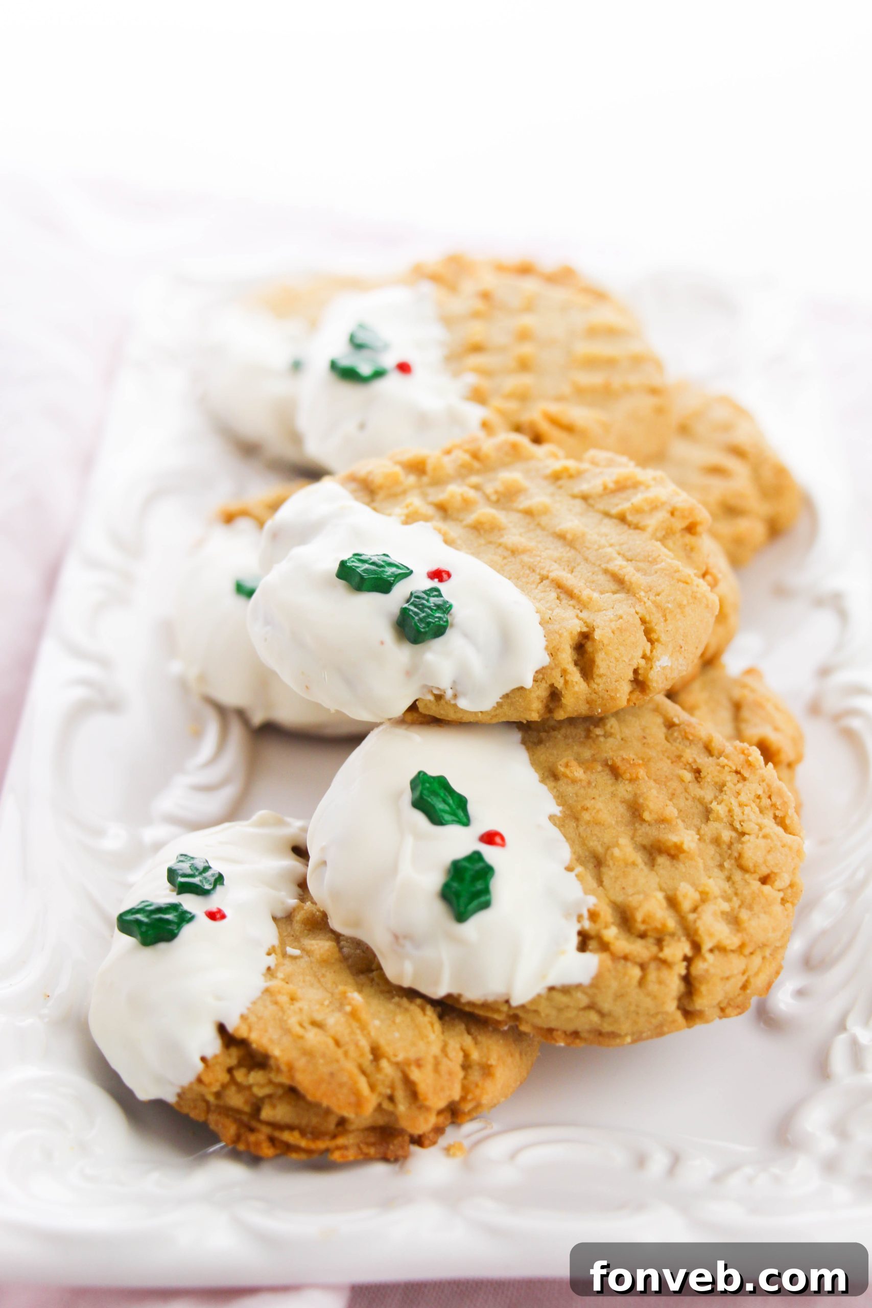Two peanut butter cookies on a wooden surface, one half-dipped in white chocolate with sprinkles, the other plain