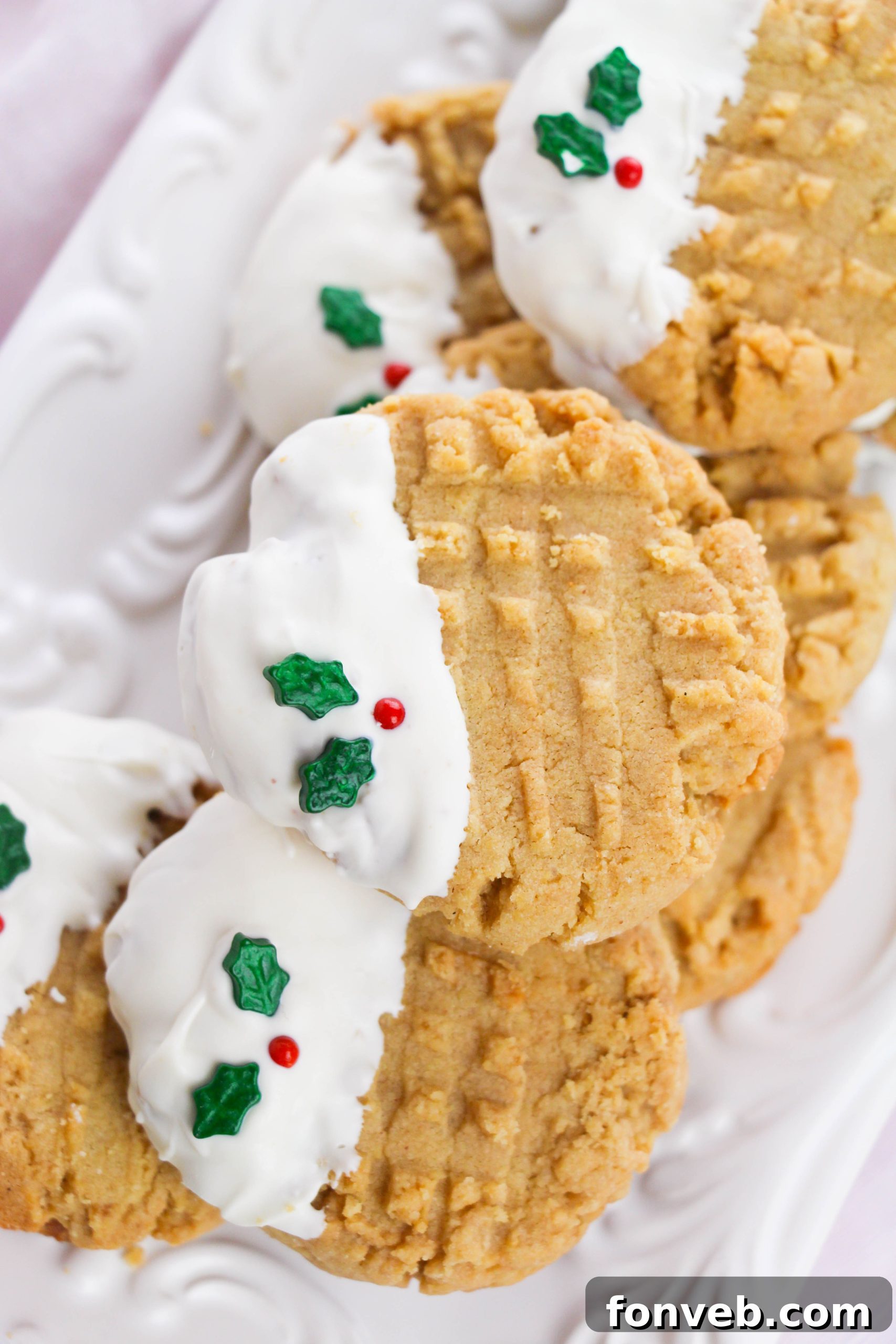A rustic wooden board filled with festive white chocolate dipped peanut butter cookies adorned with various holiday sprinkles