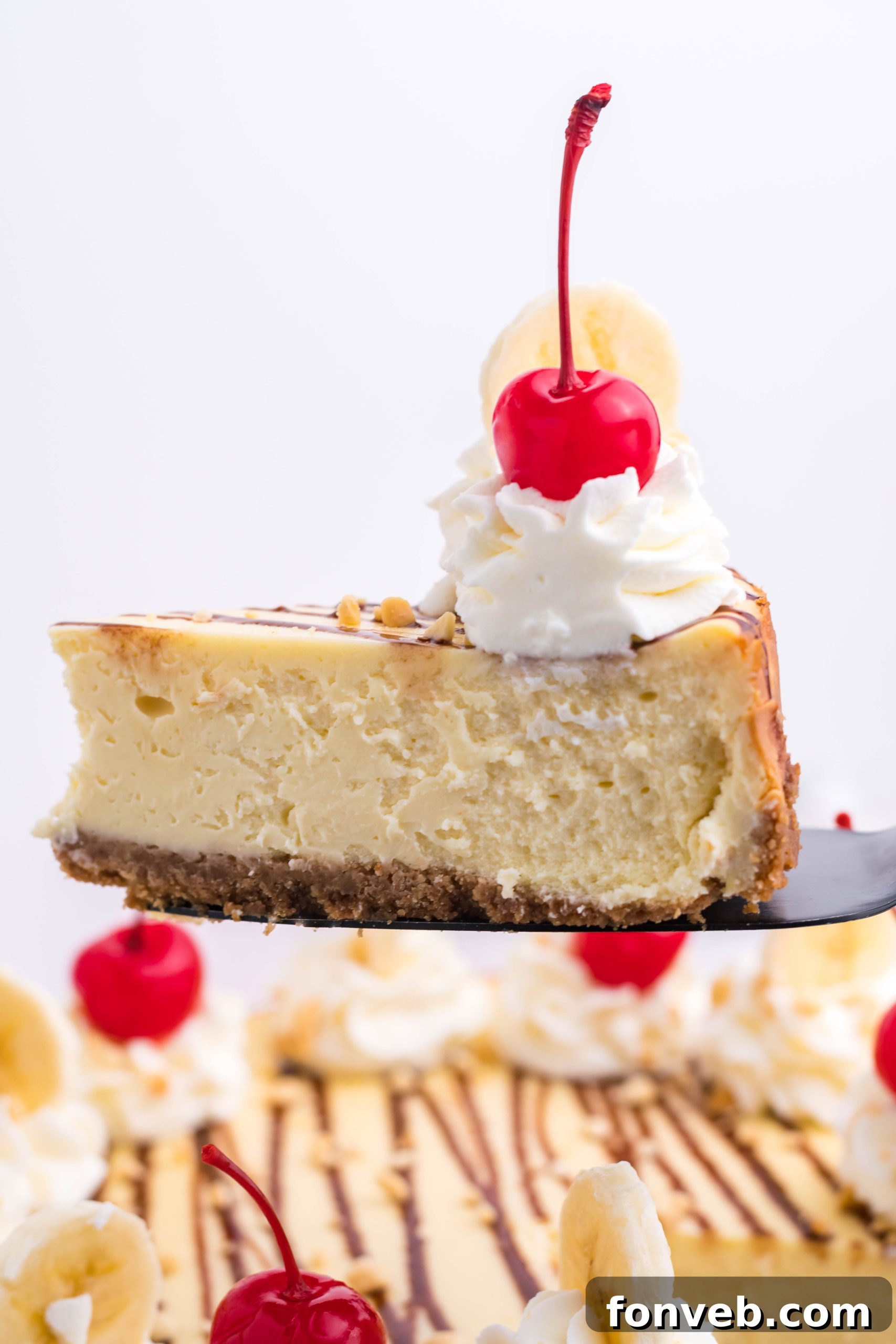 A hand drizzling chocolate syrup over a finished Banana Split Cheesecake, adding the final touch.