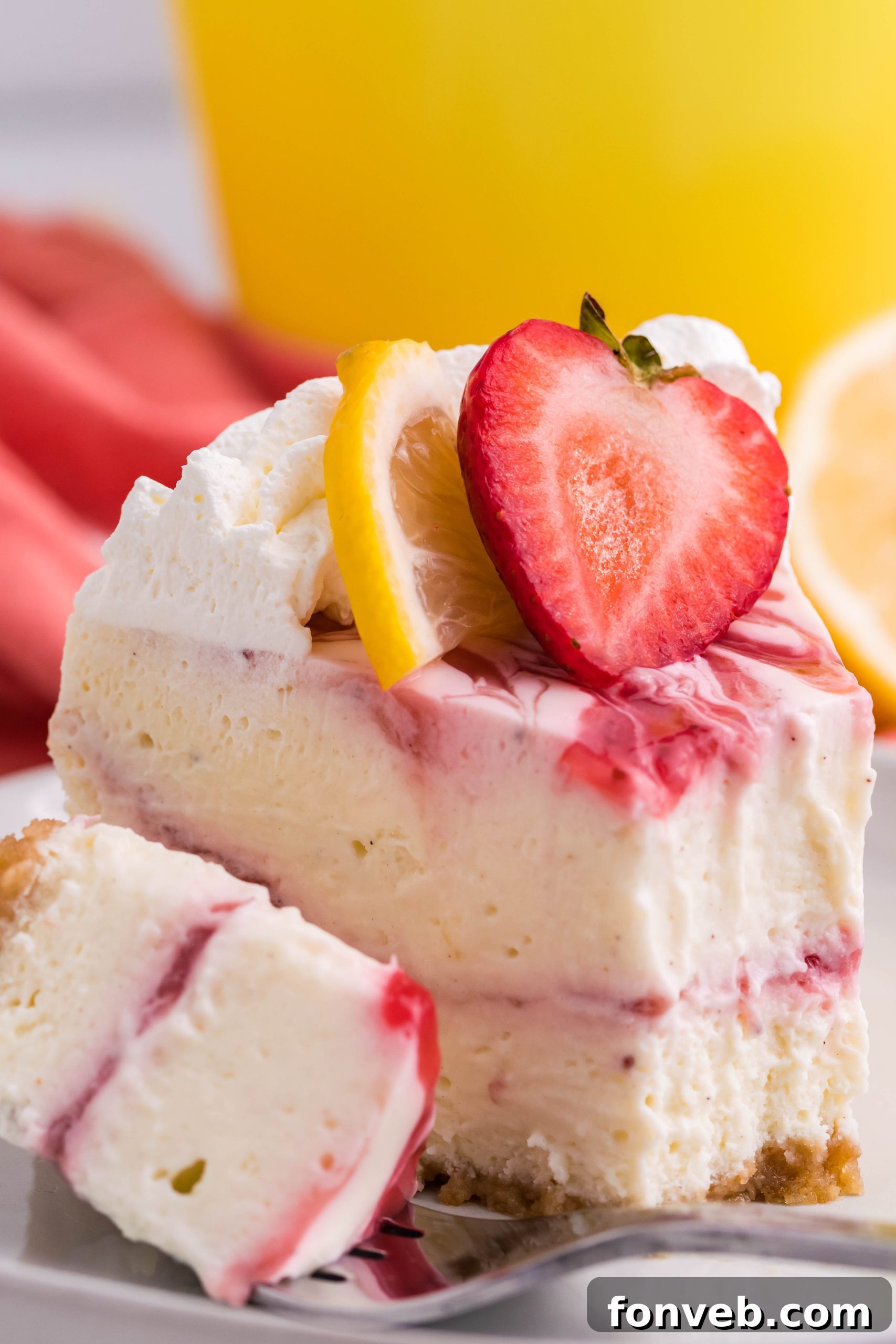 A slice of creamy strawberry lemon RumChata cheesecake on a white plate, topped with whipped cream and fresh strawberries.