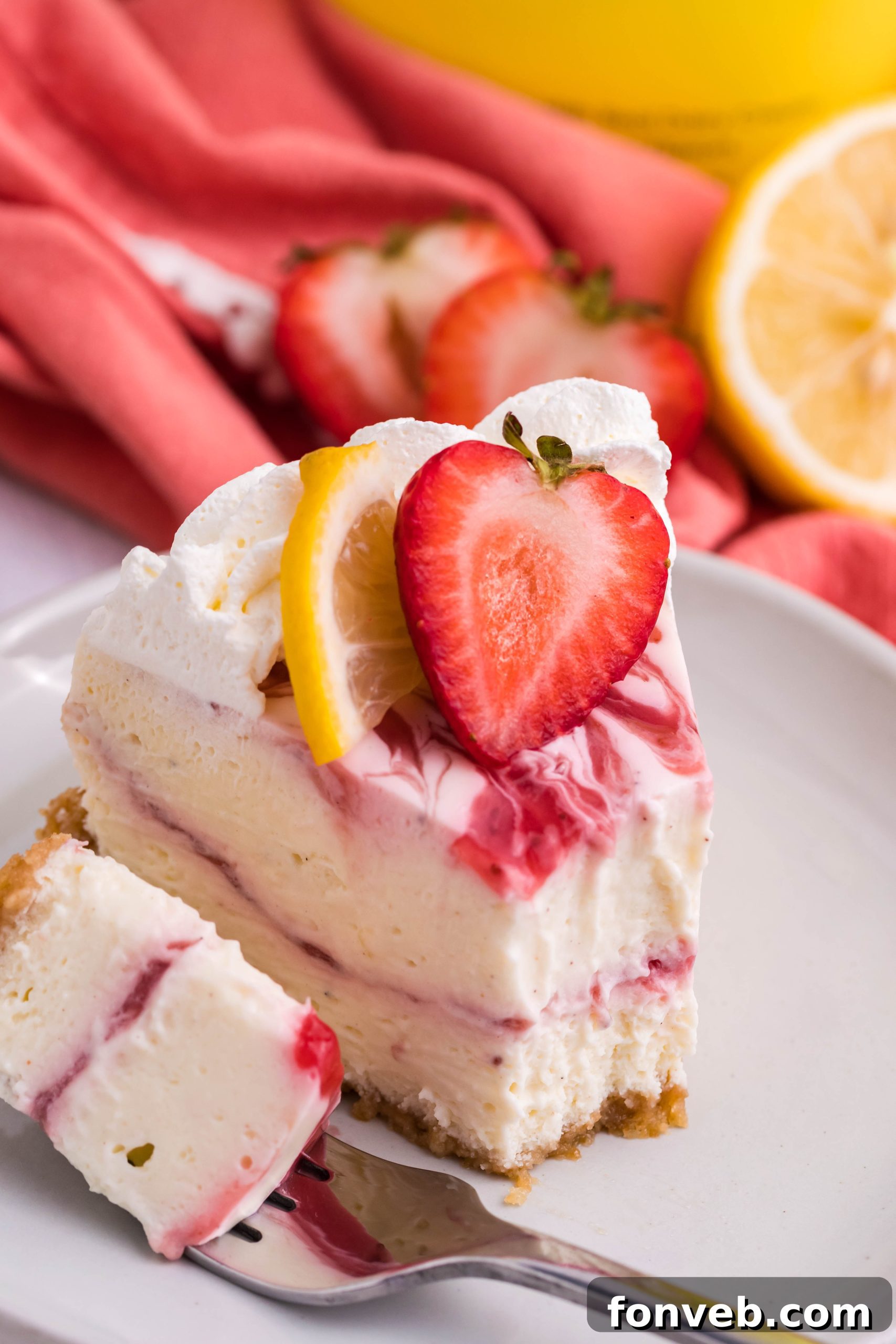 A finished slice of cheesecake topped with whipped cream, lemon, and strawberries.