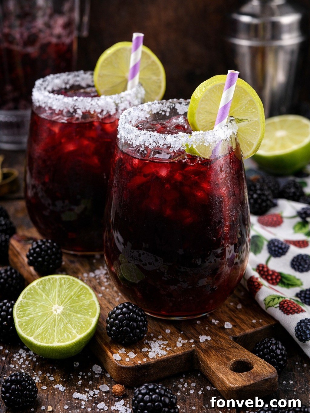 Vibrant Blackberry Margaritas on a dark wood cutting board with lime slices and fresh blackberries