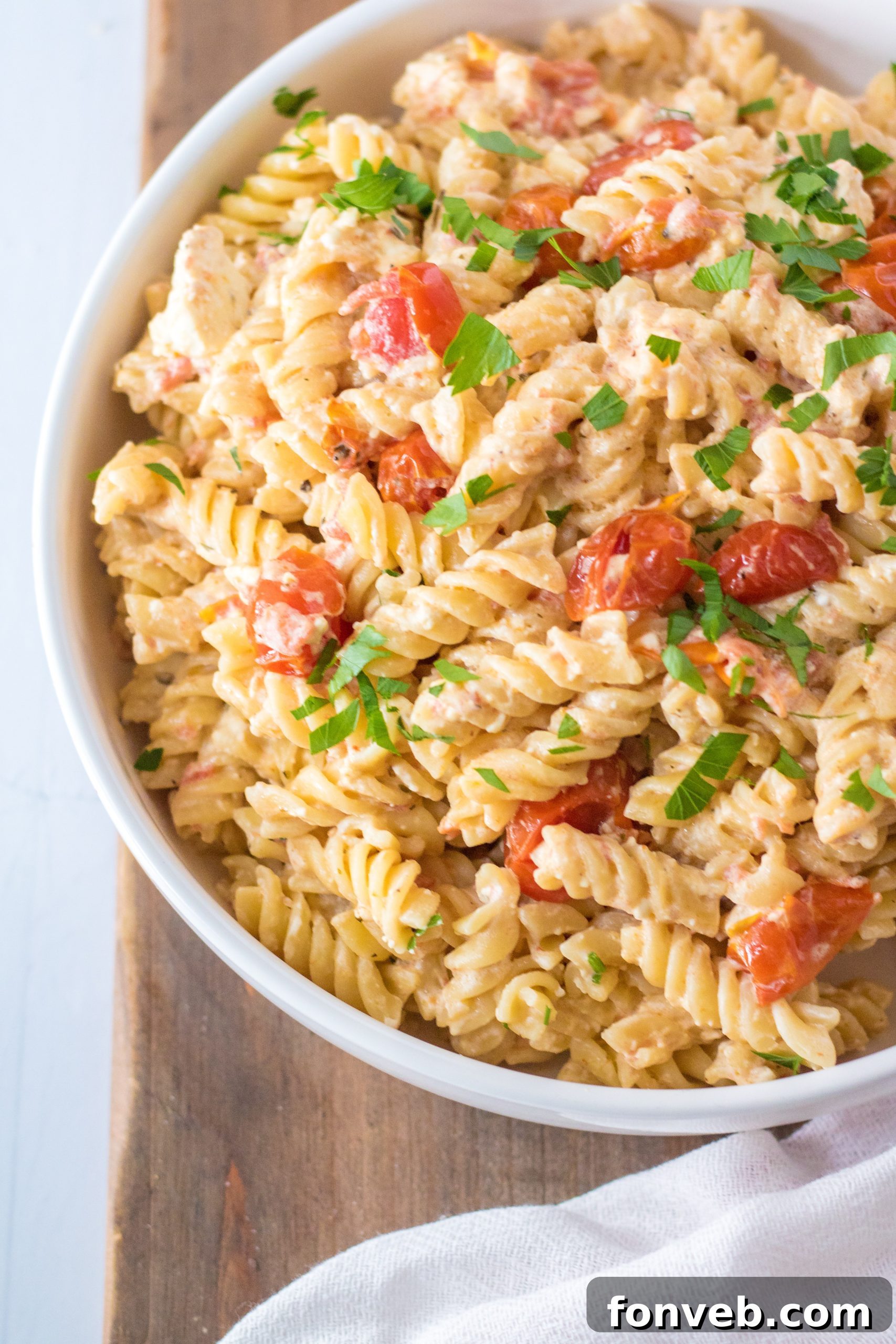 A bowl of Slow Cooker Tomato and Feta Pasta, garnished with fresh basil, placed on a wooden board with a side of toasted garlic bread and a glass of wine.