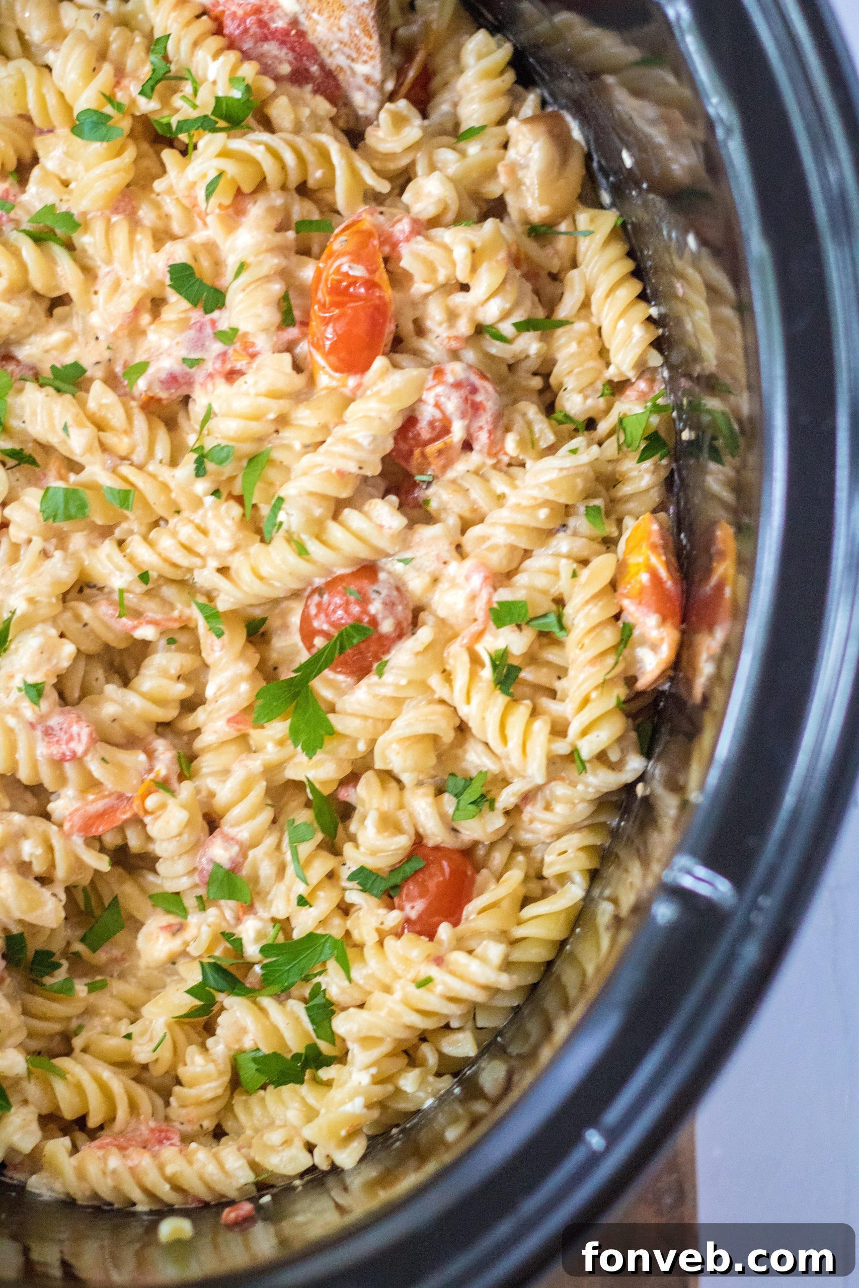 A close-up shot of the slow cooker insert, showing the rich, creamy sauce of the tomato and feta pasta after it has been cooked and stirred.