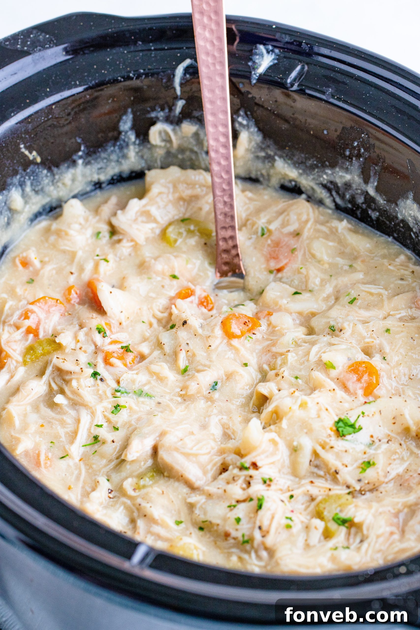 A slow cooker filled with steaming chicken and dumplings on a wooden table