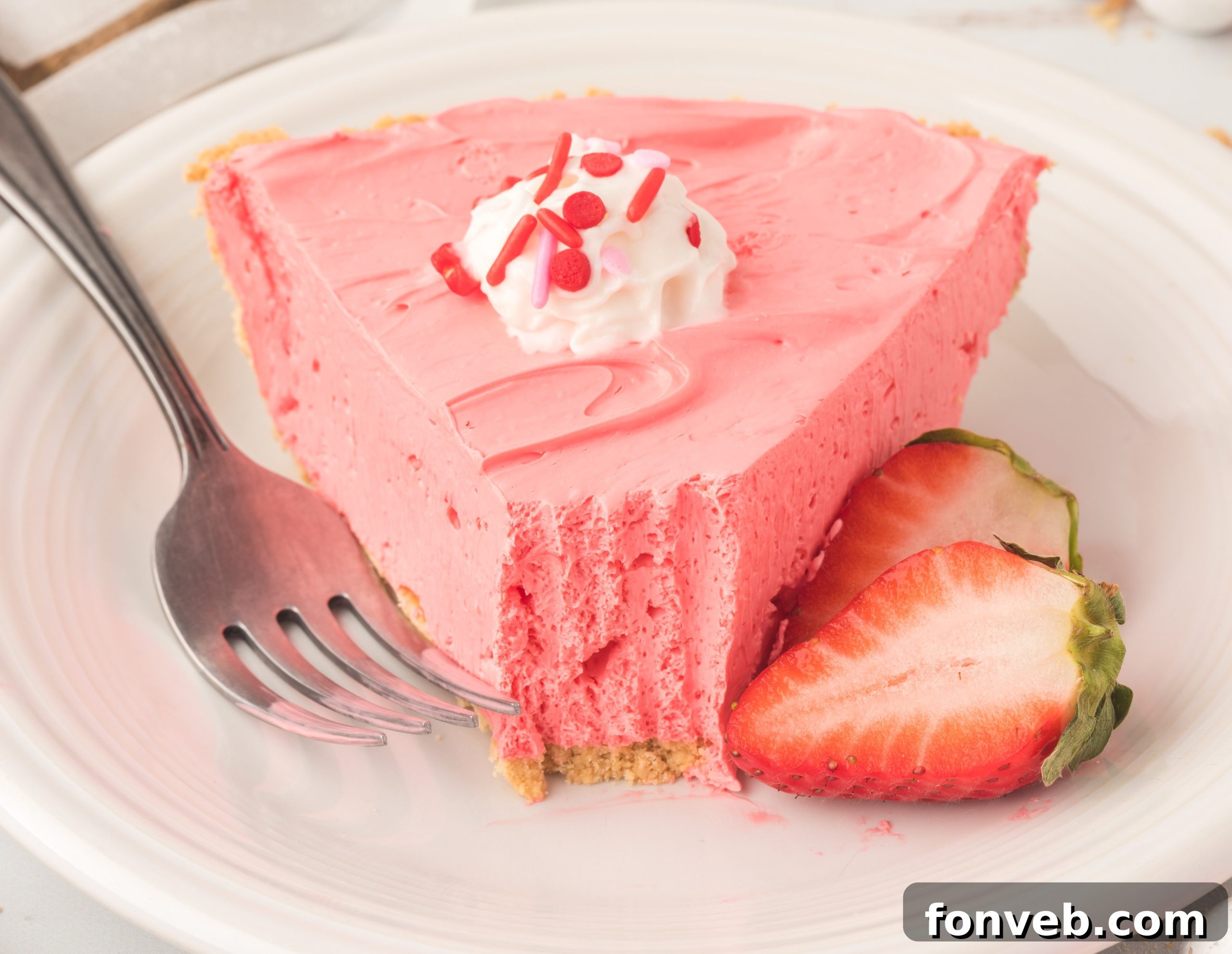 Deliciously creamy slice of Strawberry Kool-Aid Pie with whipped topping and fresh strawberries.