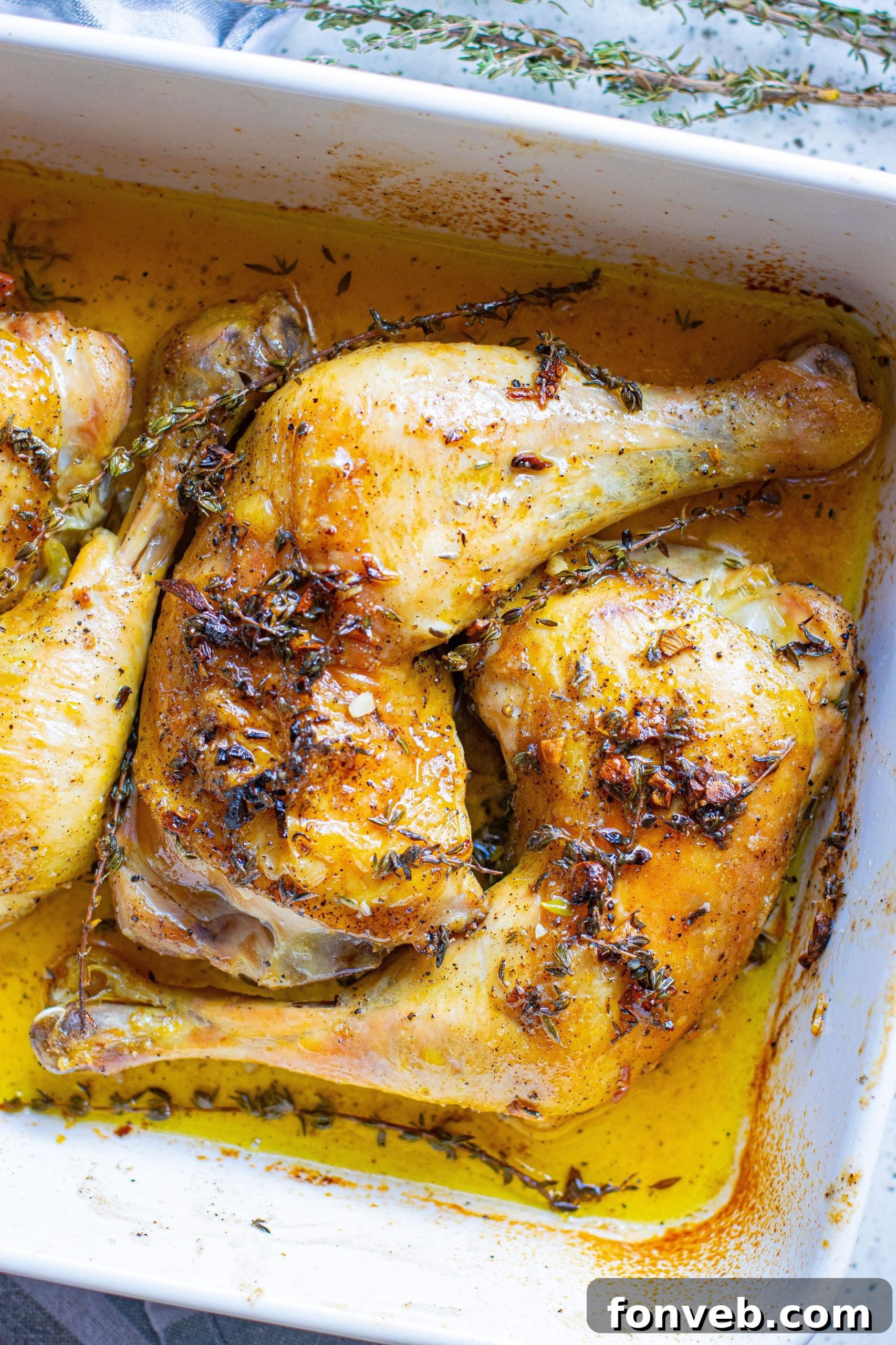 Chicken thighs generously coated with garlic butter mixture, arranged in a baking dish with thyme sprigs.