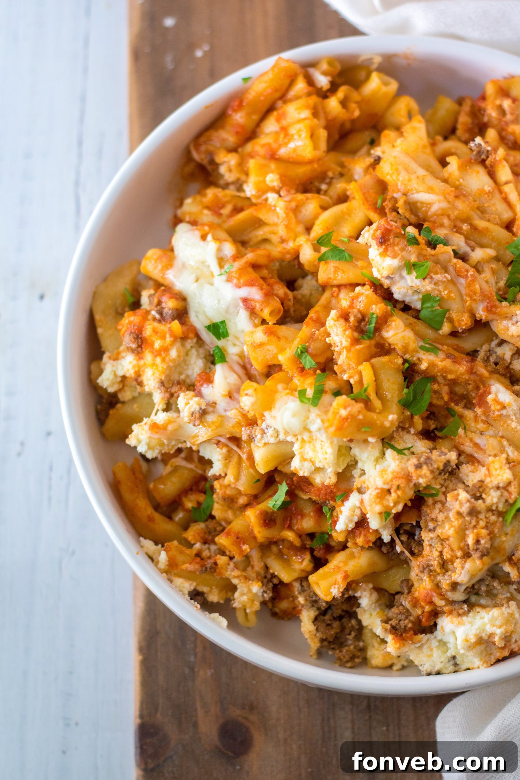 A large serving spoon scooping out Slow Cooker Cheesy Baked Pasta from a casserole dish.