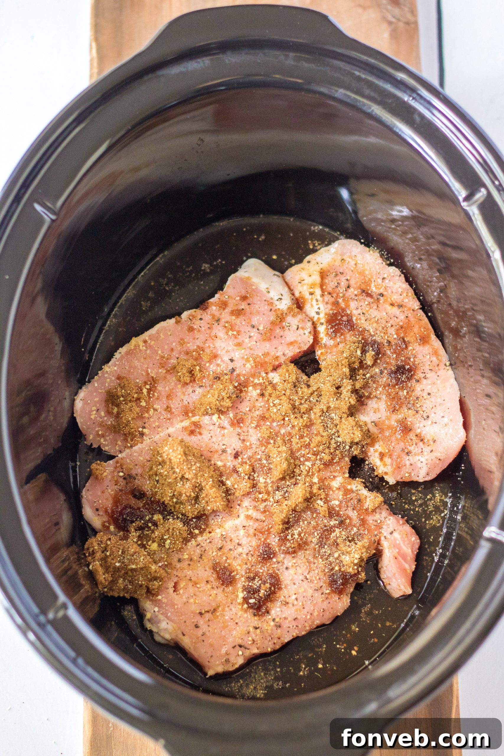 A slow cooker filled with boneless pork chops, sliced onions, and a savory sauce, ready to cook