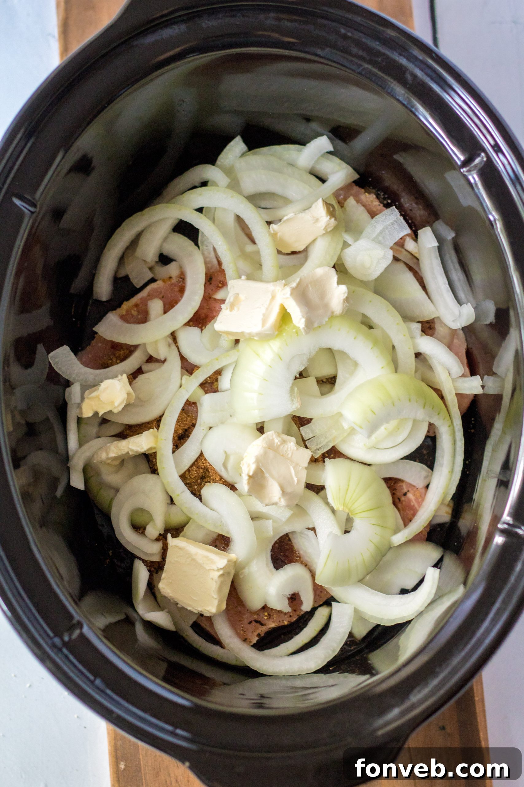 A fork piercing a tender slow cooker pork chop with a slice of onion, ready to be eaten