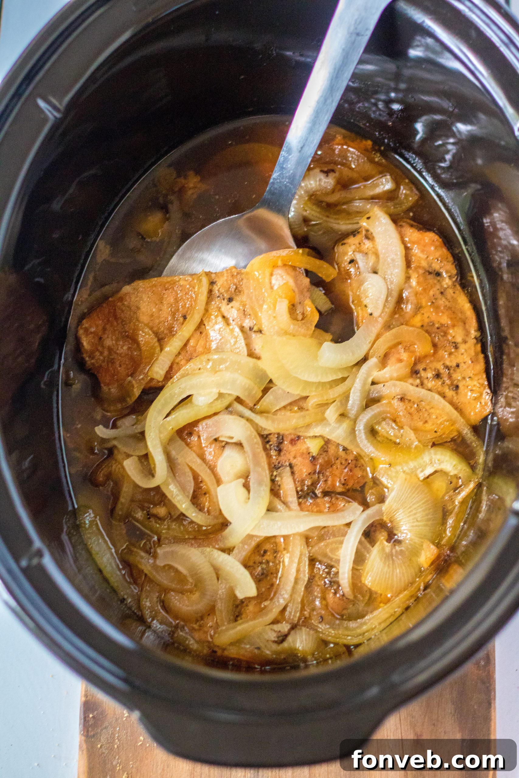 Cooked slow cooker pork chops and onions in a serving dish, garnished with fresh herbs