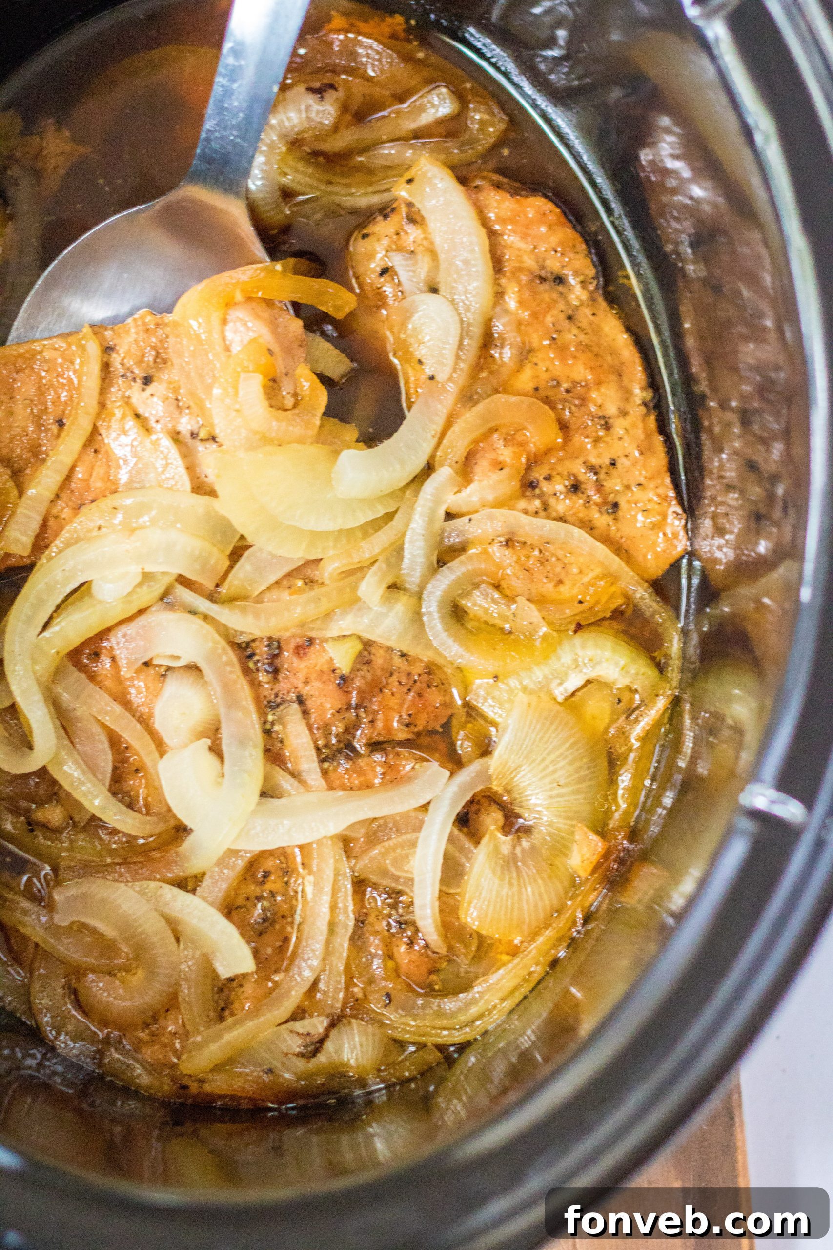 Three boneless pork chops stacked on a cutting board, ready for the slow cooker