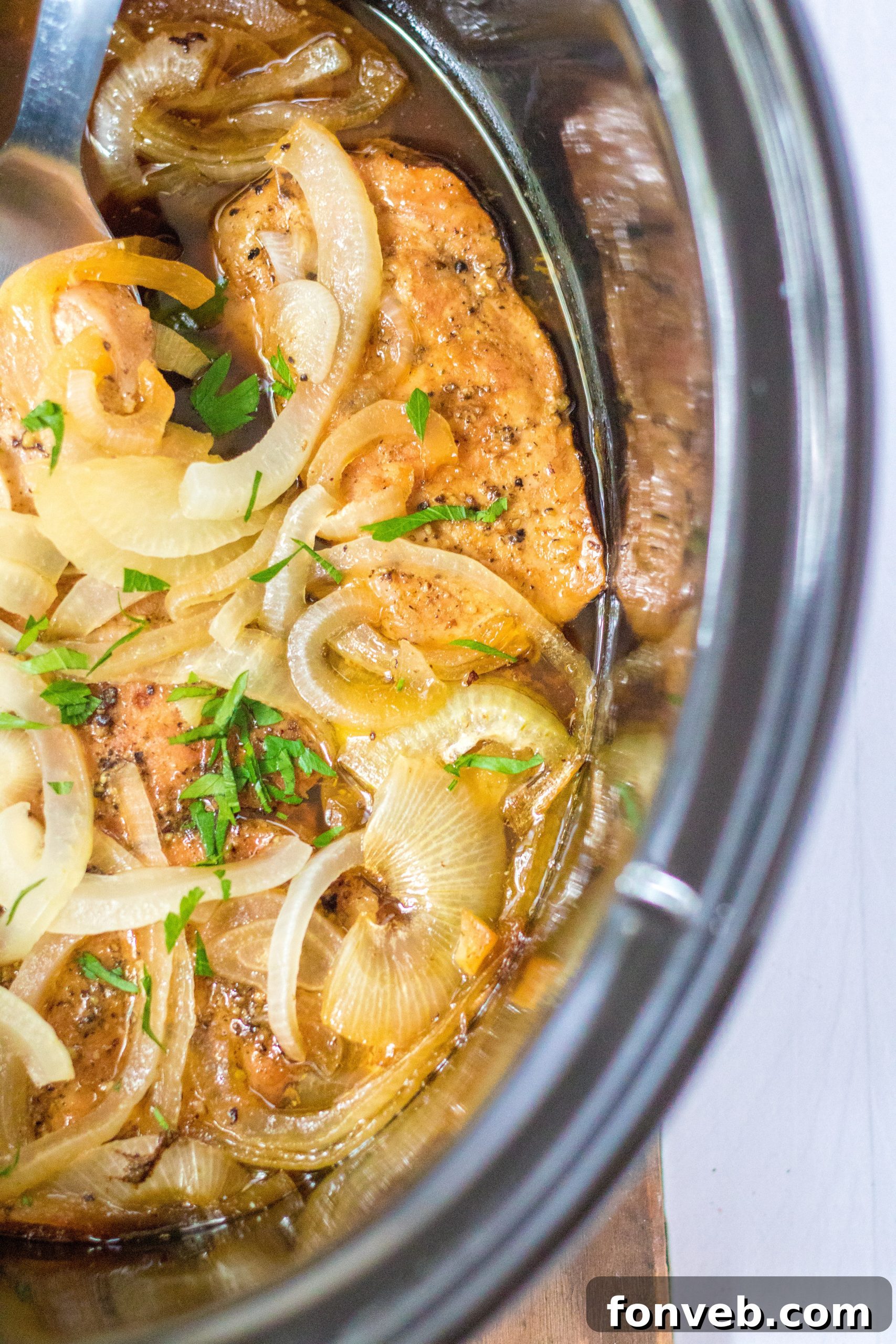 A slow cooker lid being removed, revealing steaming, cooked pork chops and onions