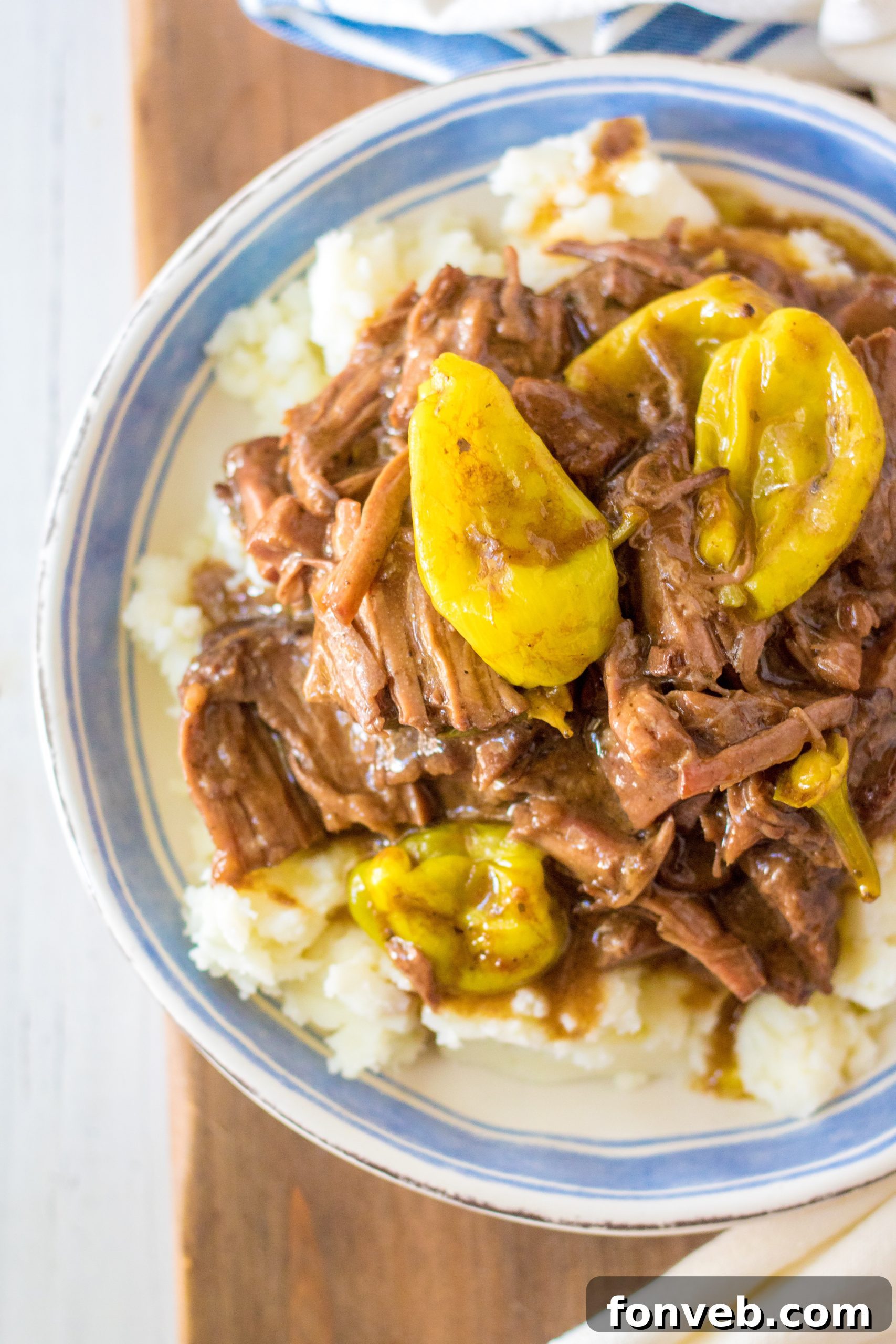Melt-in-Your-Mouth Slow Cooker Mississippi Pot Roast 13 An overhead shot of Slow Cooker Mississippi Pot Roast in a serving dish with mashed potatoes and green beans.