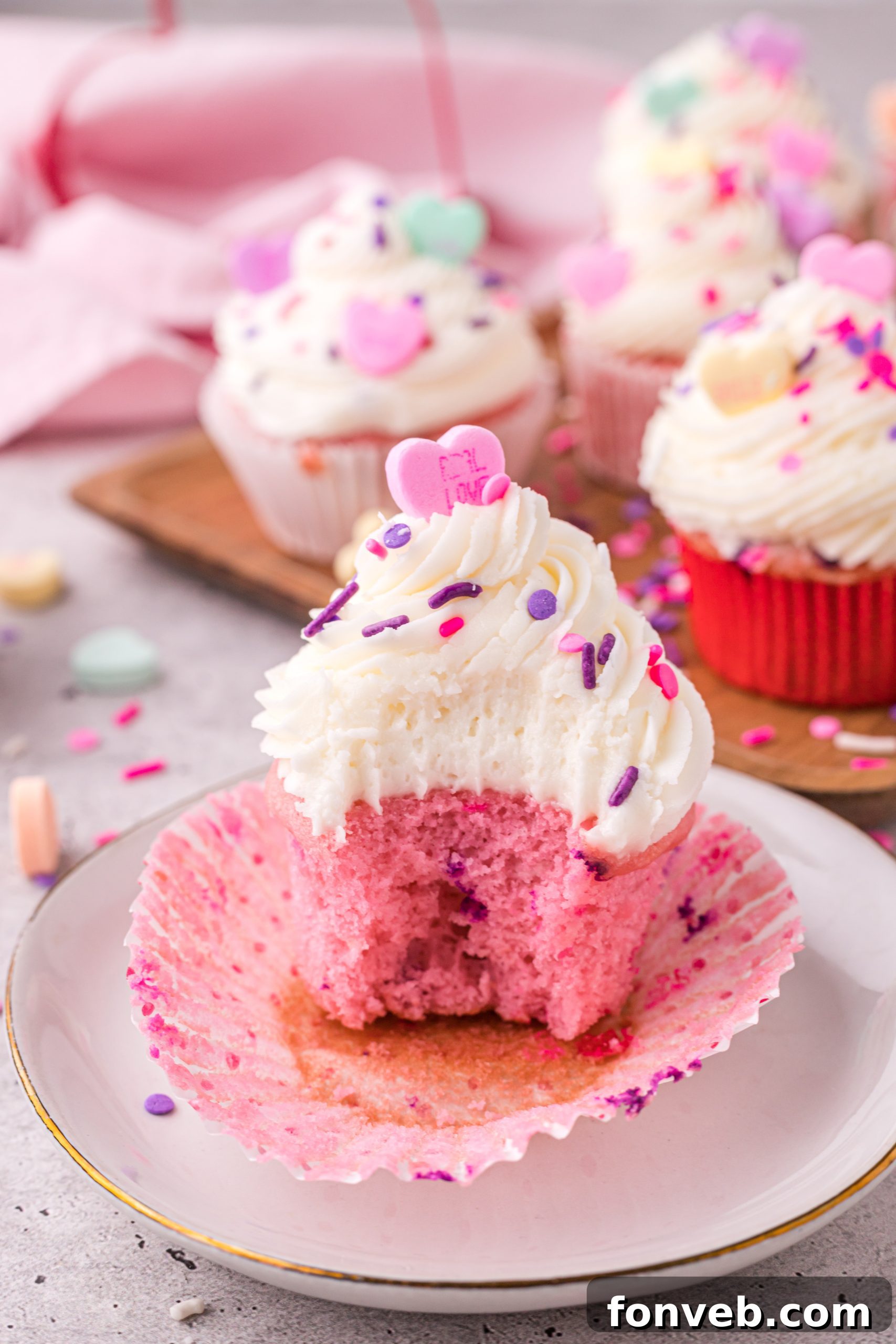 Blushing Velvet Vanilla Cupcakes 8 A trio of pink velvet cupcakes with vanilla buttercream and various sprinkles, arranged on a cooling rack.