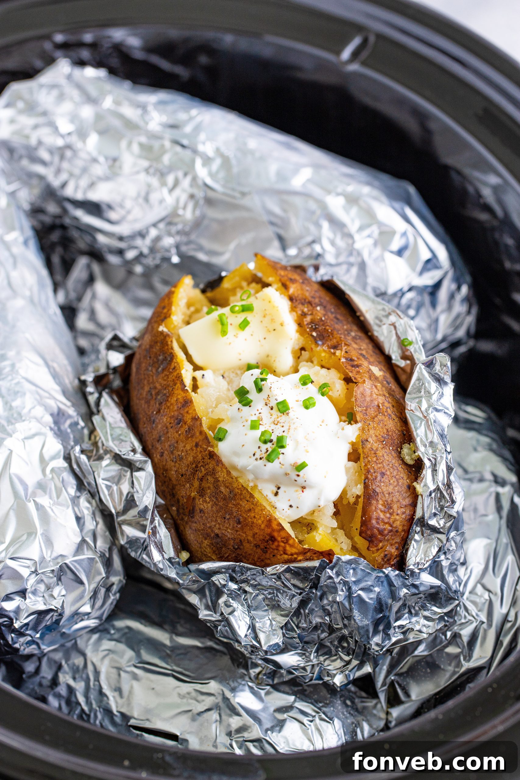 Two hands holding a freshly cooked, unwrapped slow cooker baked potato, showcasing its warmth and tenderness