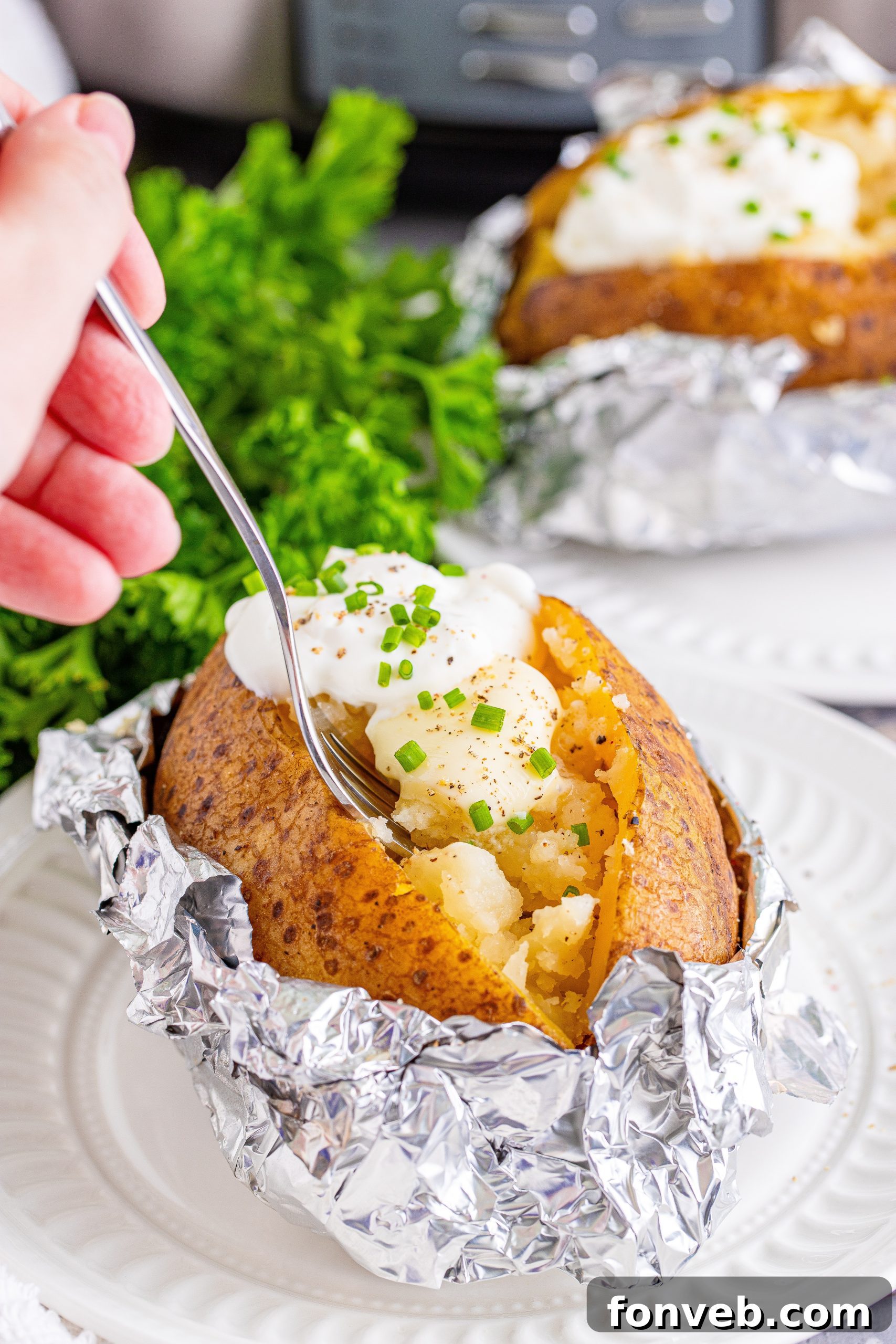 A single perfectly cooked slow cooker baked potato, generously topped with sour cream and fresh chives, and sprinkled with black pepper