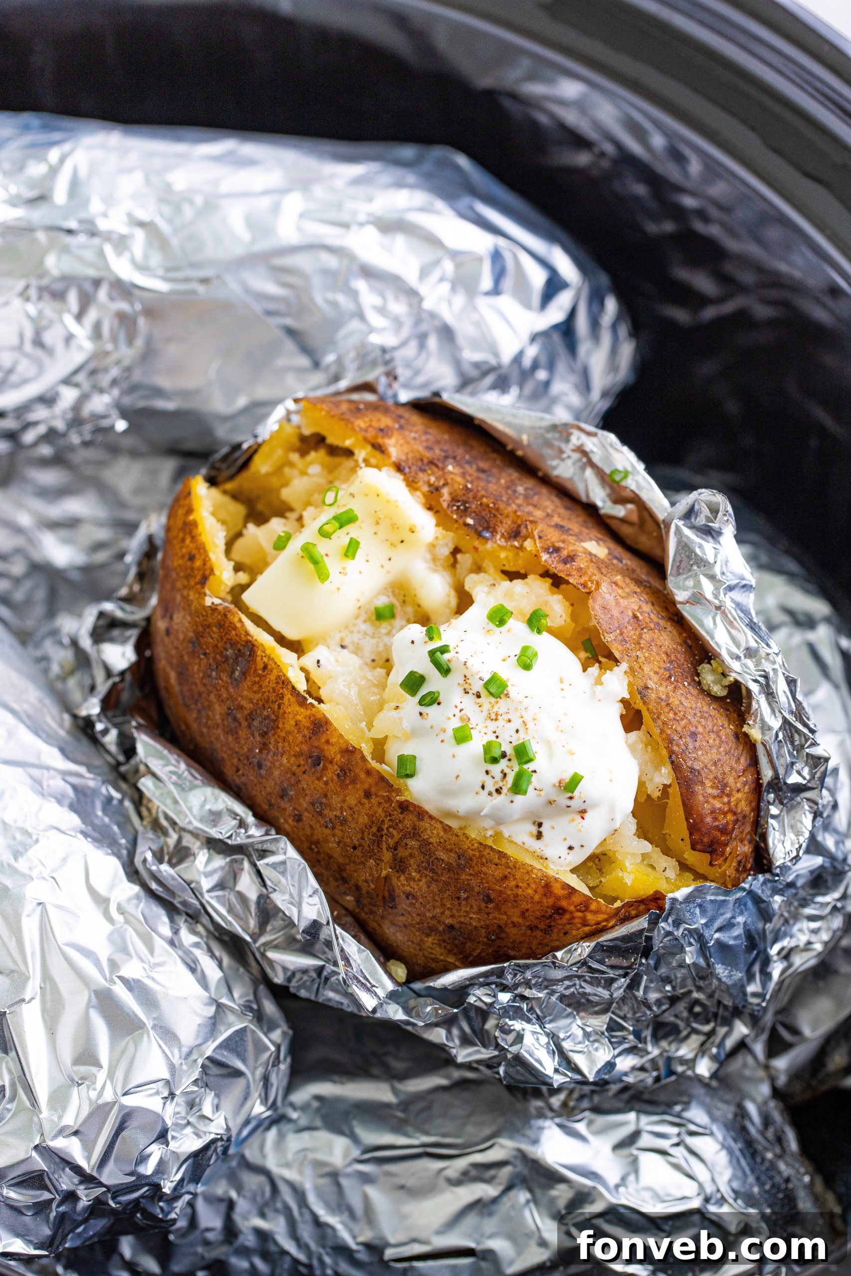 Hands carefully unwrapping a perfectly cooked slow cooker baked potato from its aluminum foil casing