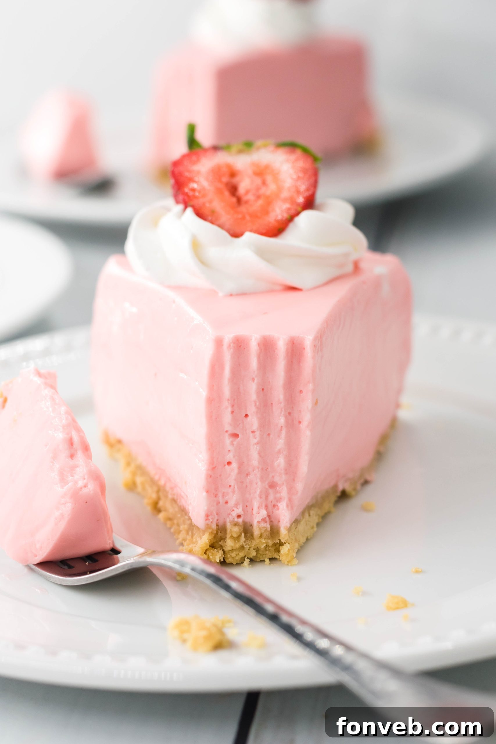 Luscious No-Bake Strawberry Cheesecake 2 A slice of creamy No Bake Strawberry Cheesecake with fresh strawberries and whipped cream on top, served on a white plate.