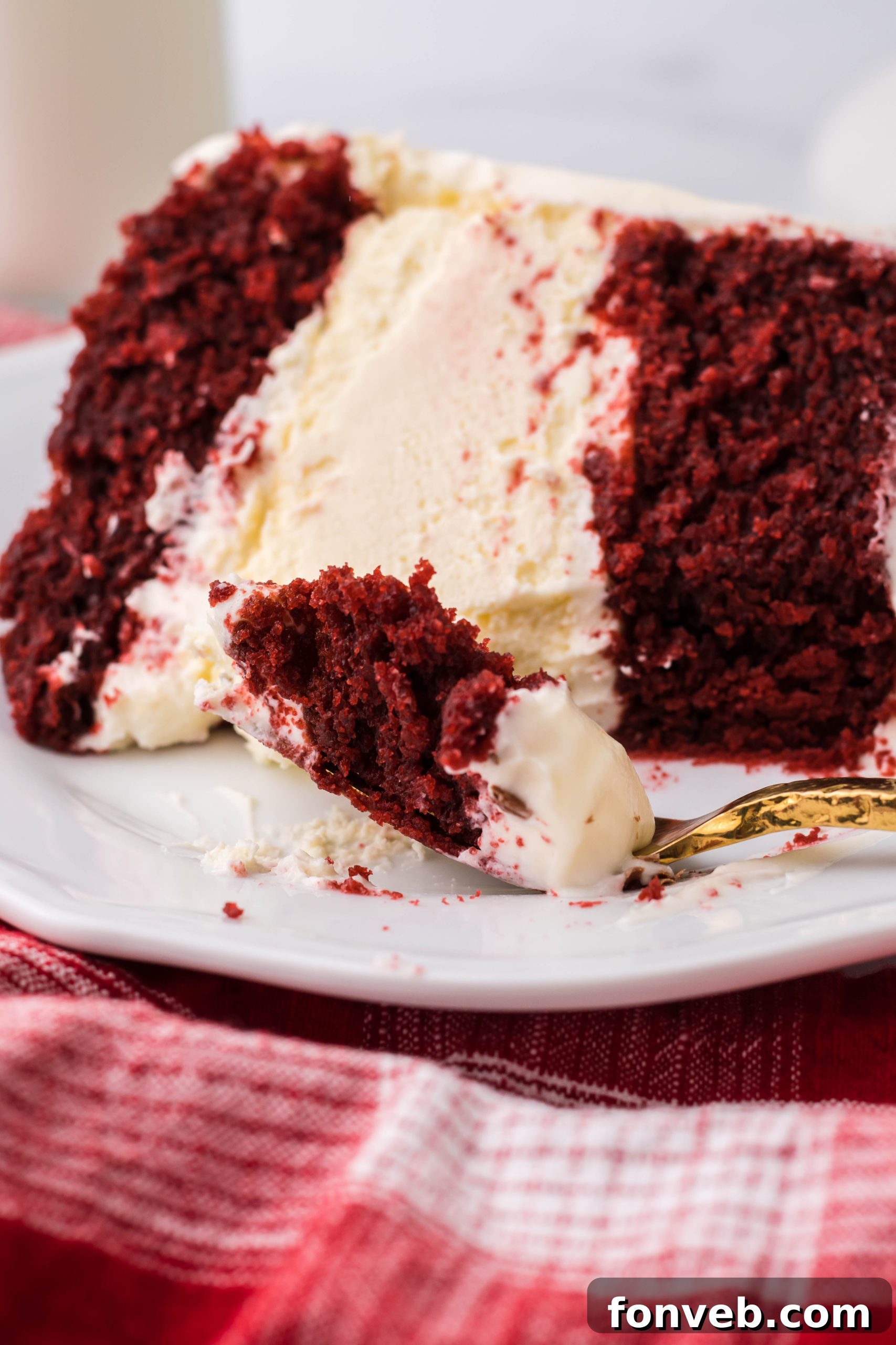 A slice of Red Velvet Cheesecake Cake with creamy frosting, showing the distinct red cake layers and a white cheesecake layer in the middle.