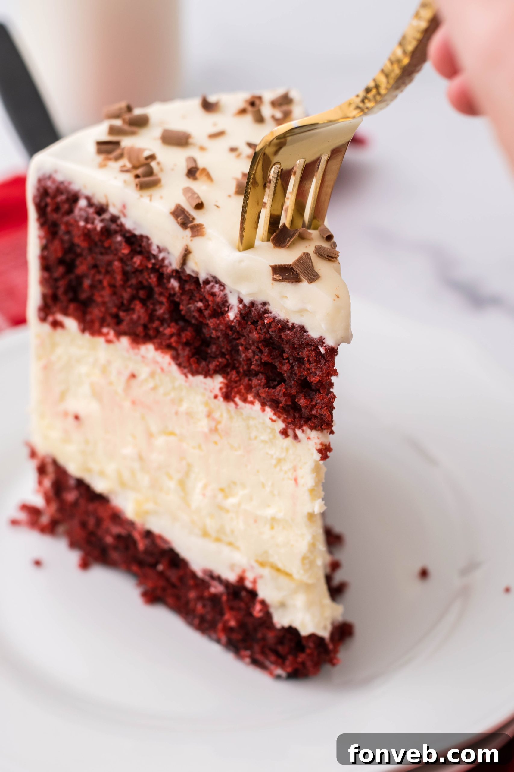 A close-up of the Red Velvet Cheesecake Cake slice, showing the layers and chocolate shavings clearly.