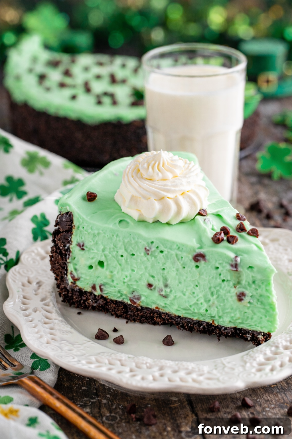 No Bake Mint Chocolate Chip Cheesecake on a white plate with St. Patrick's Day decor, garnished with chocolate chips and mint leaves.