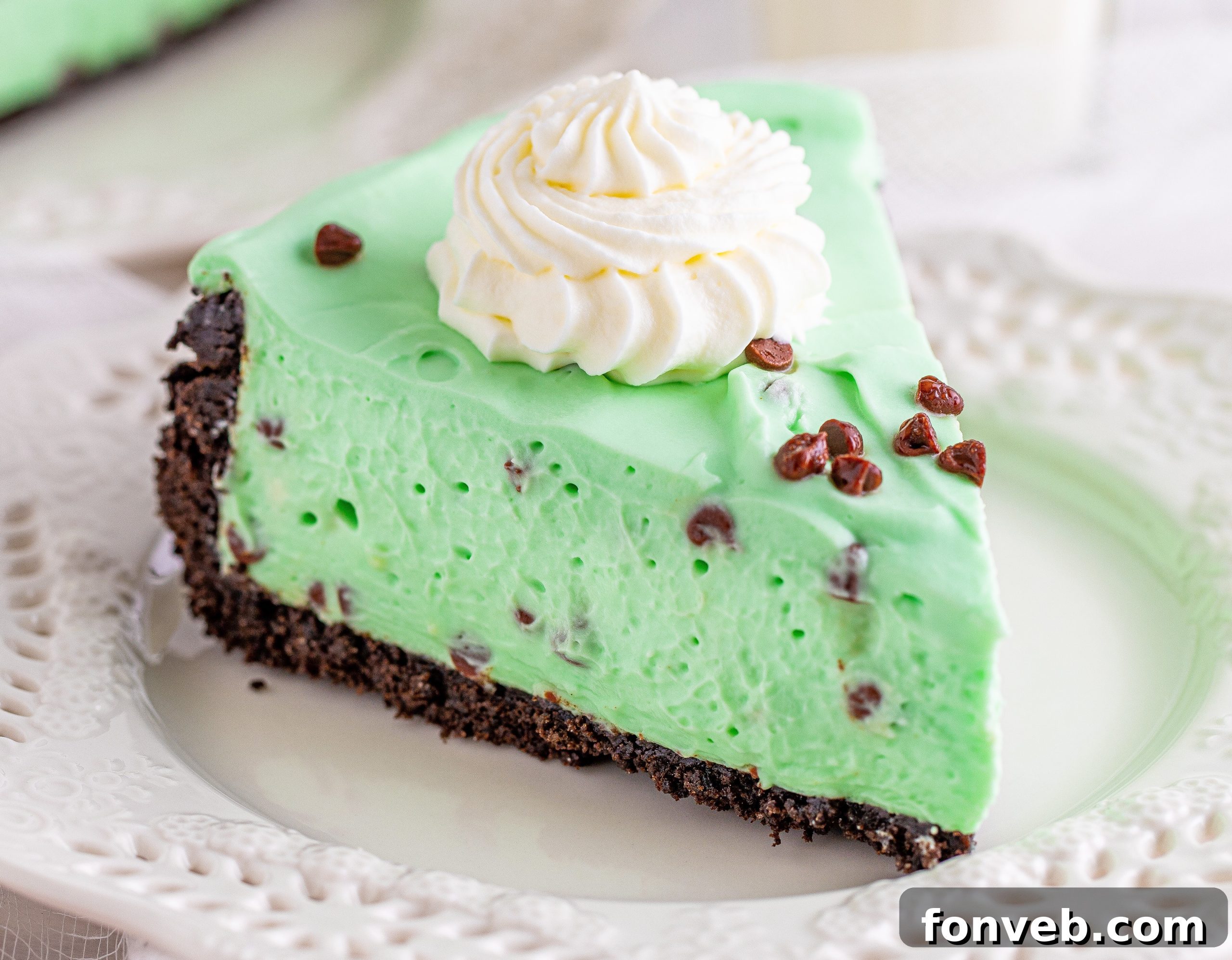 A close-up of a single slice of No Bake Mint Chocolate Chip Cheesecake on a white plate, showing the distinct layers and vibrant green color.