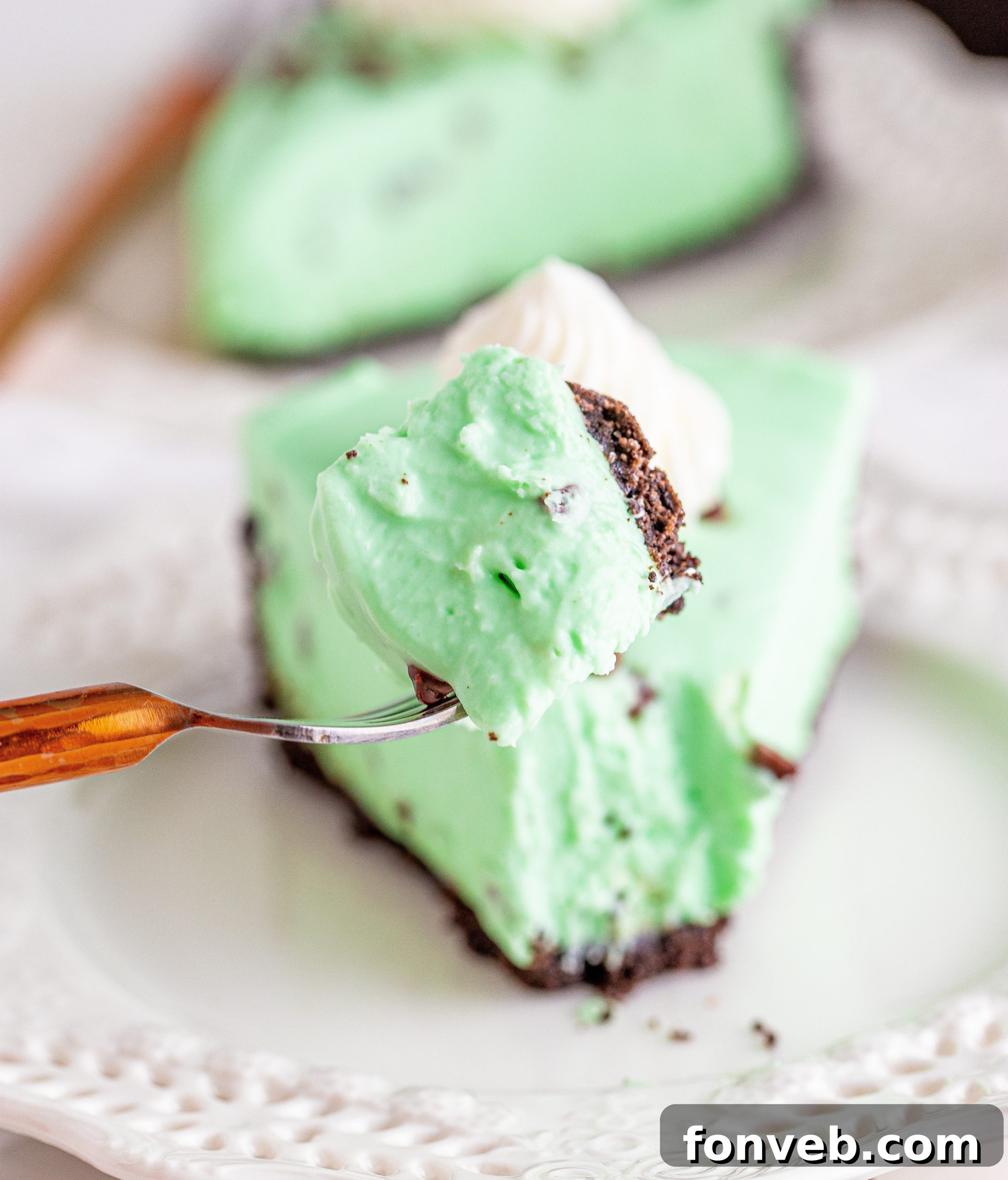A visually appealing slice of No Bake Mint Chocolate Chip Cheesecake on a plate with scattered chocolate chips around.