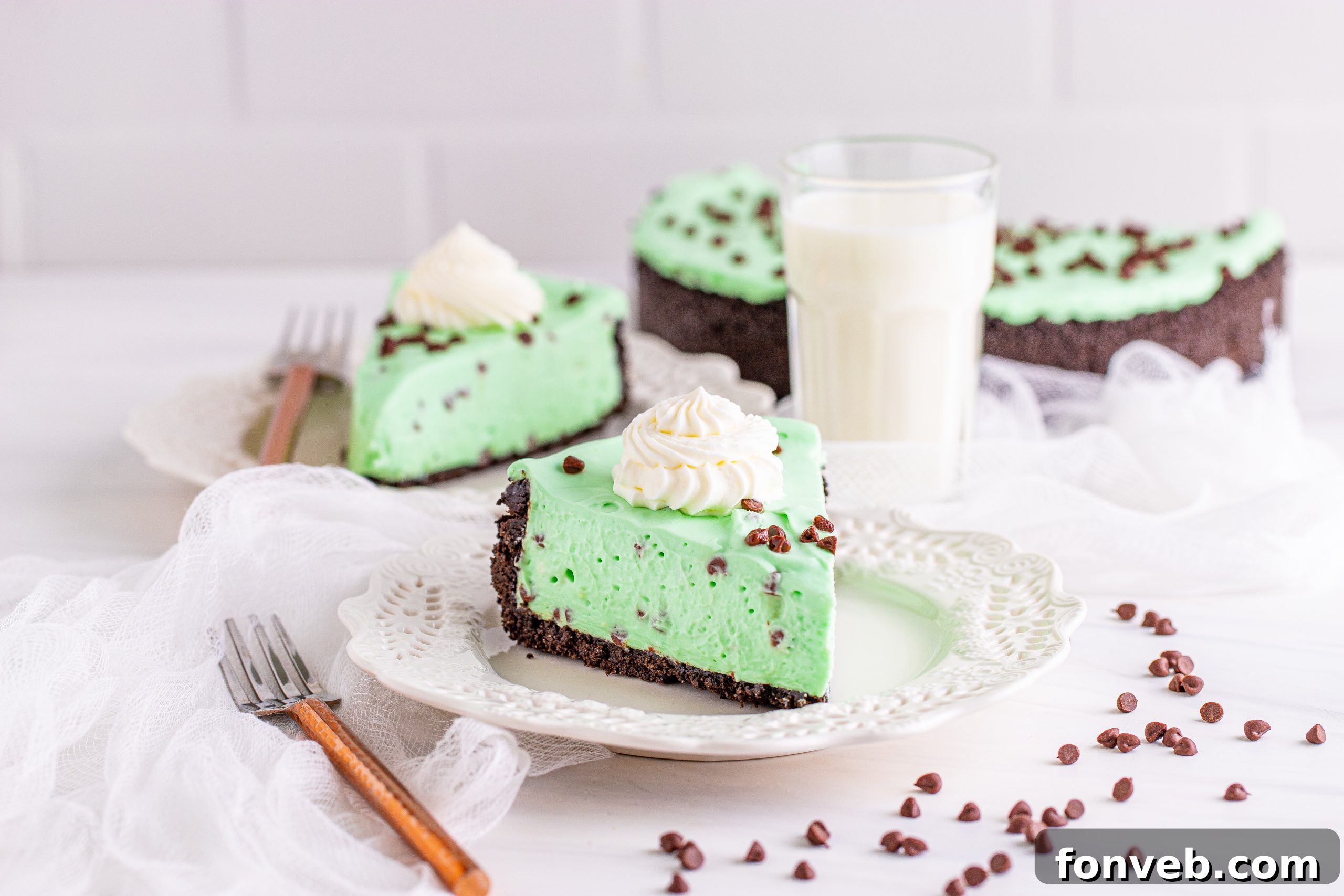 An overhead shot of a single slice of No Bake Mint Chocolate Chip Cheesecake on a white plate, adorned with whipped cream and chocolate shavings.