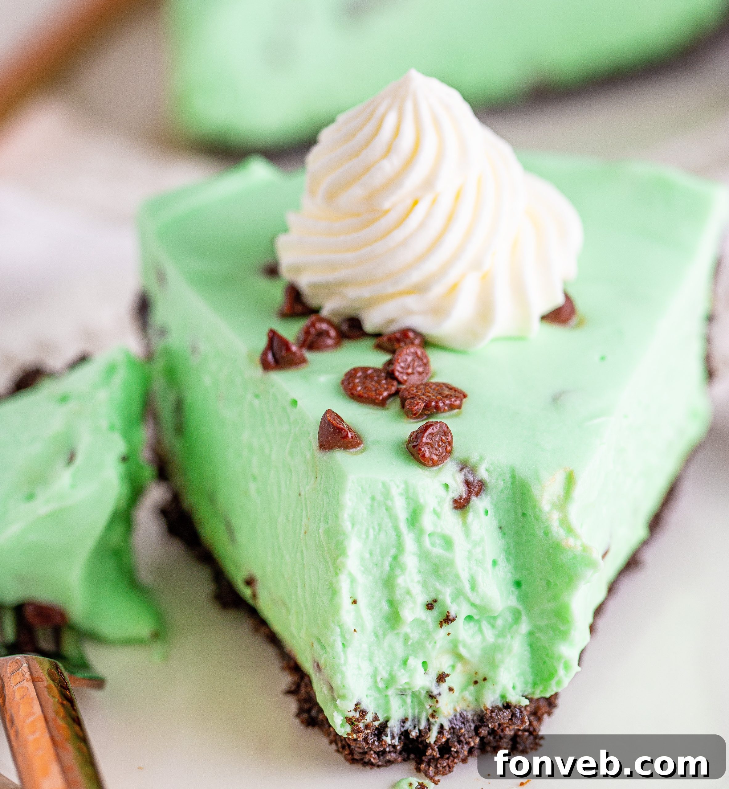 A visually striking close-up of a slice of No Bake Mint Chocolate Chip Cheesecake, featuring a clear view of the crunchy crust and fluffy green filling.