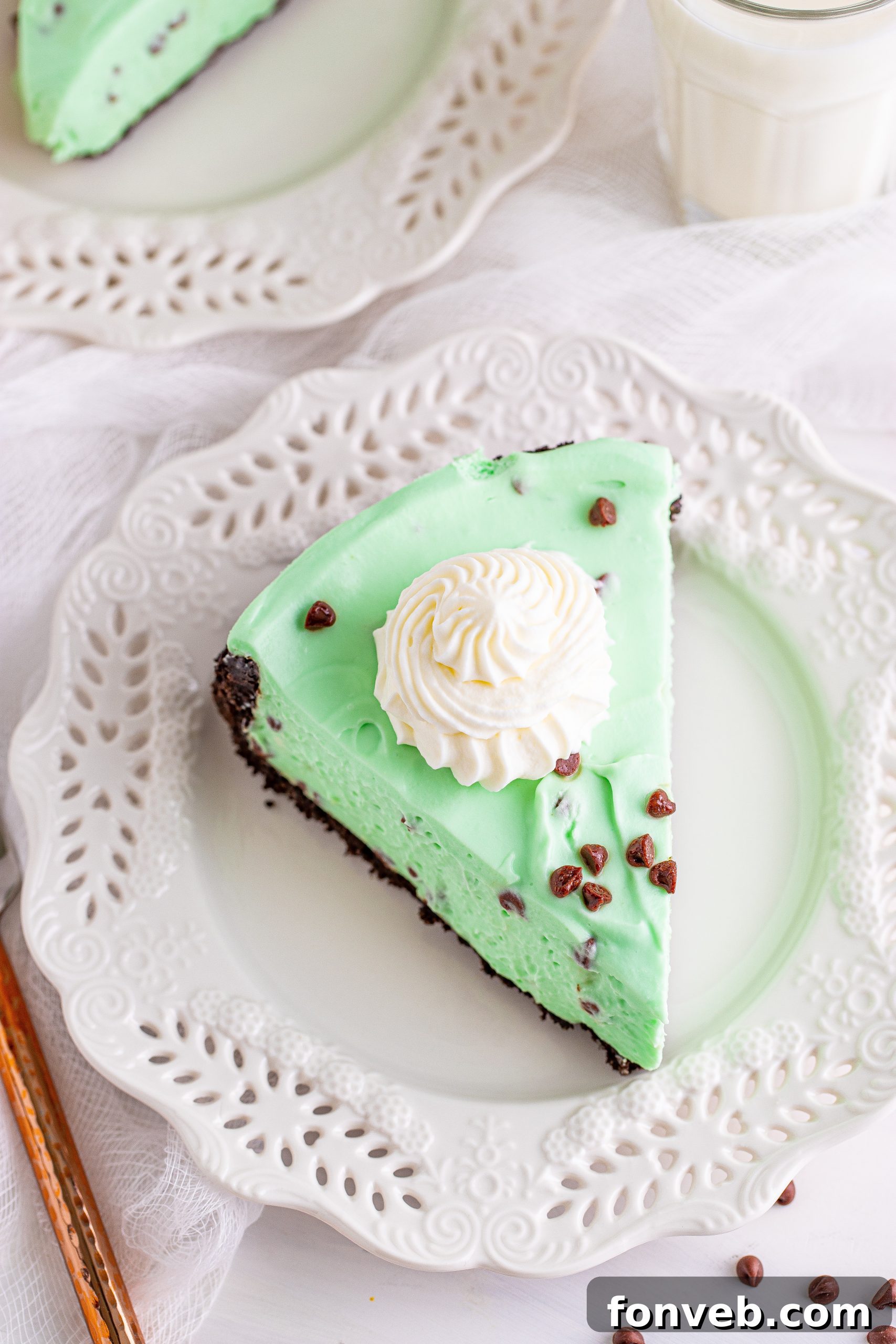 A vibrant green slice of No Bake Mint Chocolate Chip Cheesecake with a delicate swirl of whipped cream and a sprinkle of chocolate chips on top.