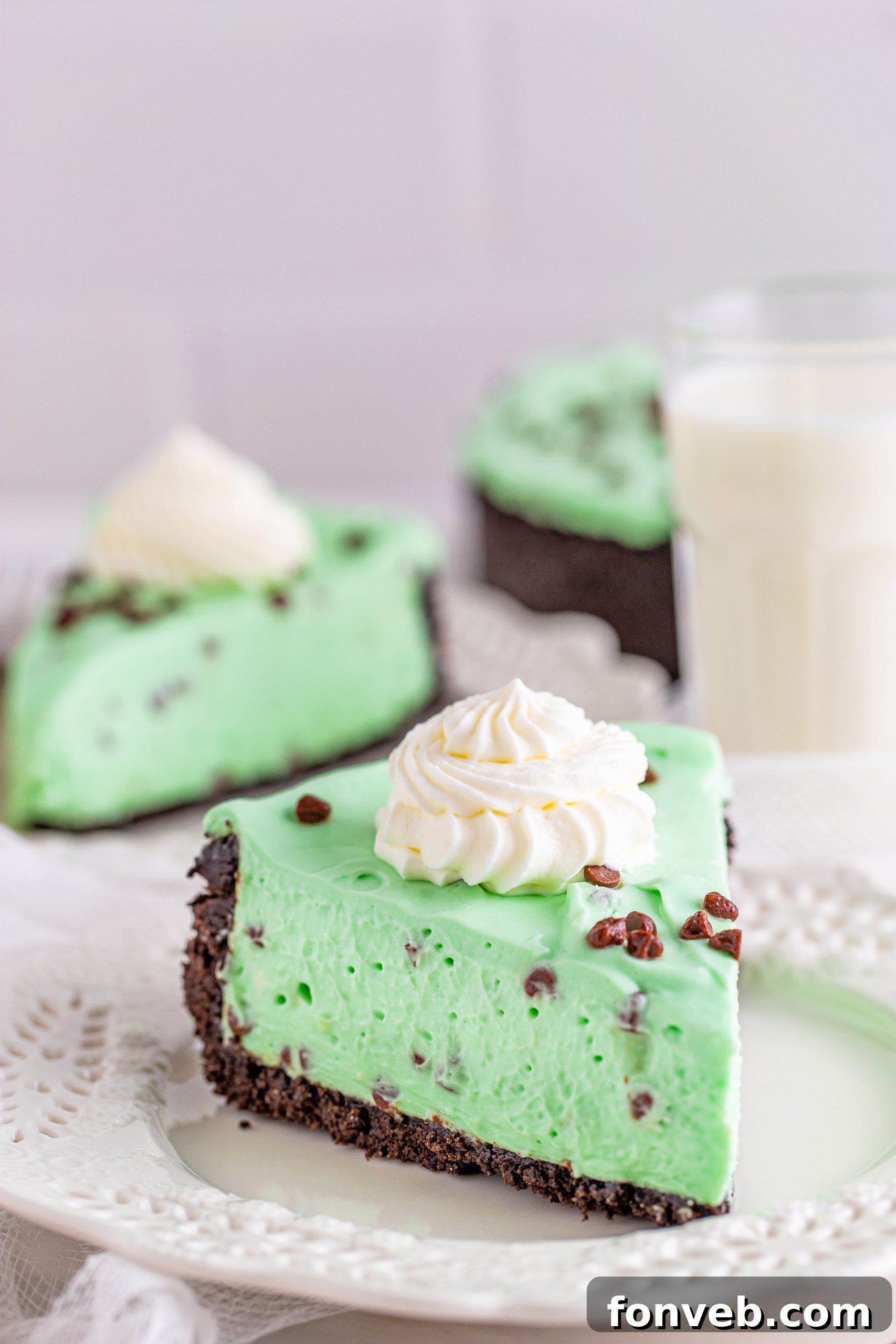 A beautiful close-up shot of the No Bake Mint Chocolate Chip Cheesecake, garnished with mint leaves, chocolate chips, and mini chocolate sticks.
