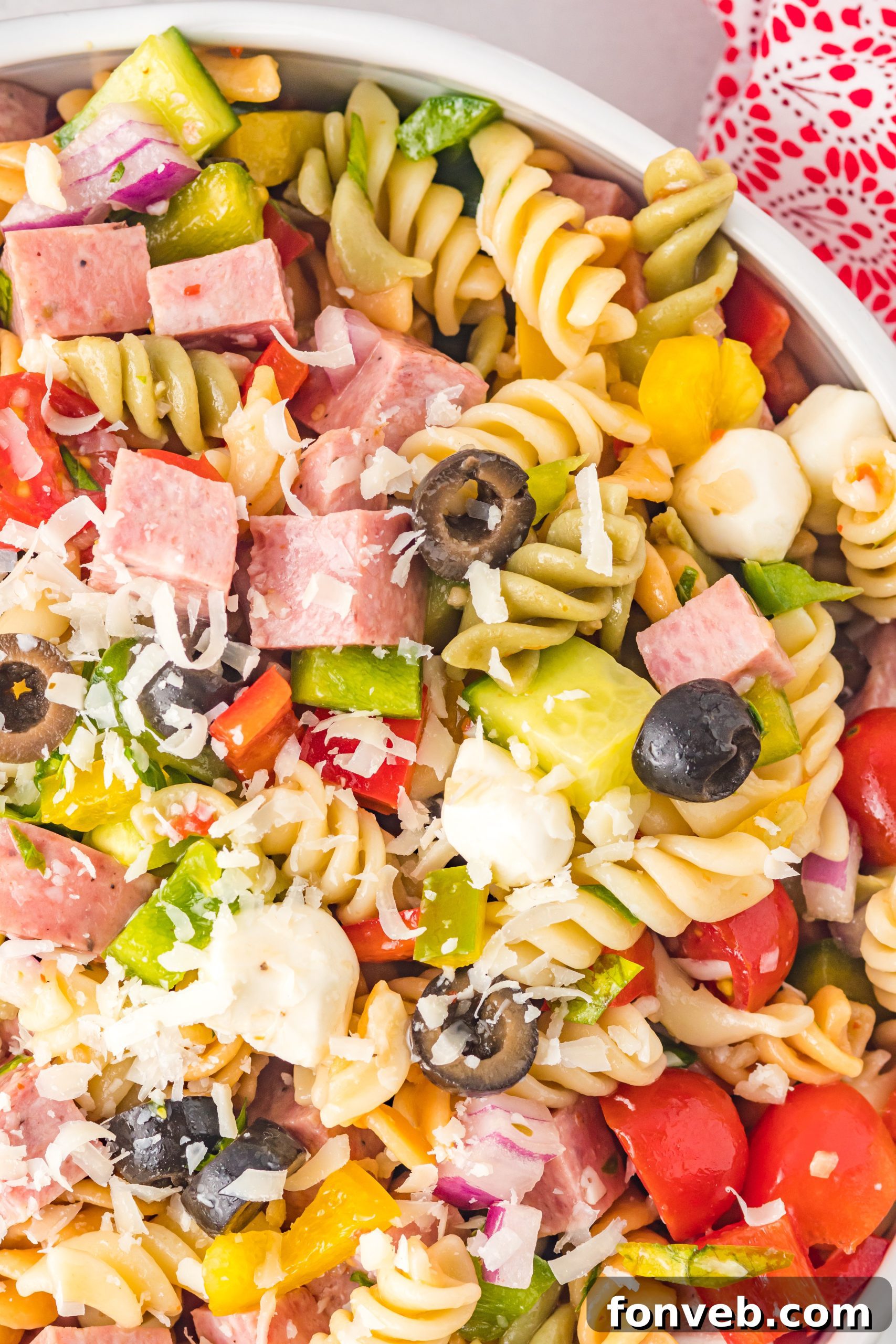 A close-up shot of the Classic Italian Pasta Salad in a large serving bowl, highlighting the colorful rotini pasta, various vegetables, meats, and cheese pearls mixed with dressing.
