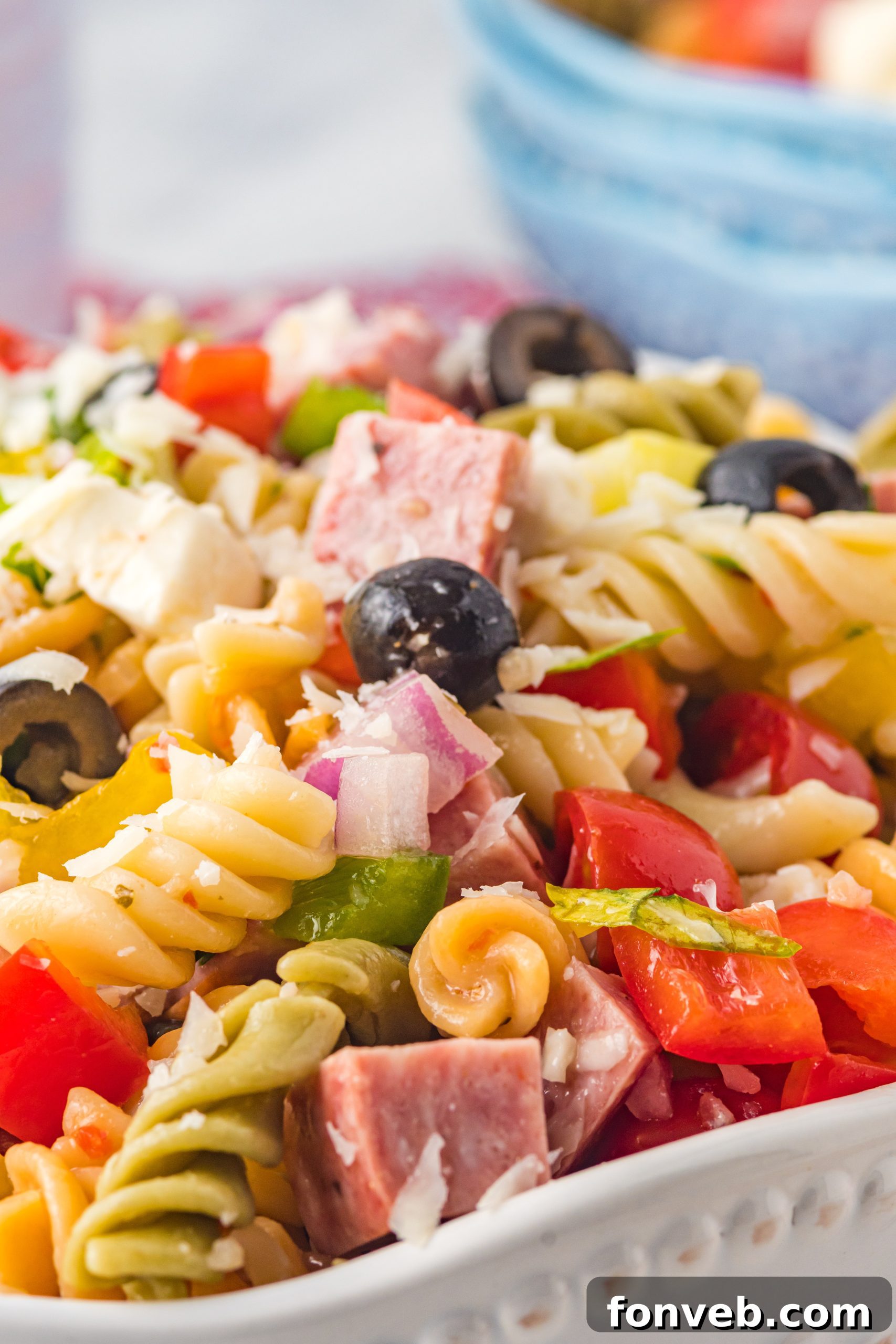 A close-up of the Italian Pasta Salad being mixed in a large bowl, ensuring all ingredients are evenly coated with dressing.