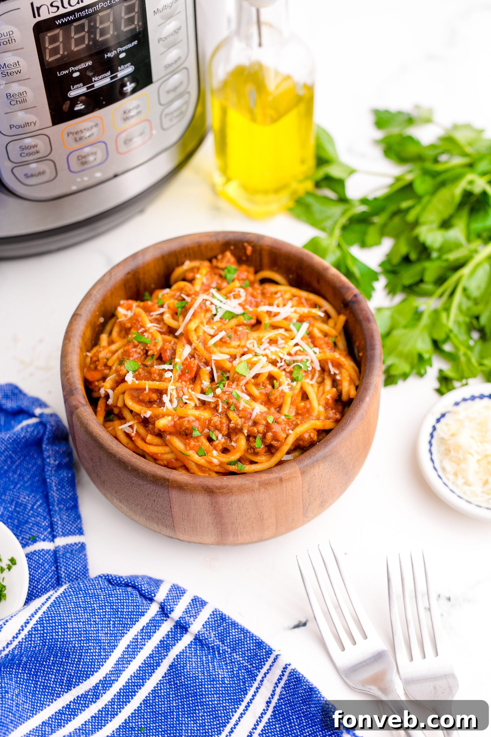 Instant Pot Spaghetti in a wooden bowl with a blue napkin next to the bowl , a fork , the instant pot in the background and a small bowl of parmesan cheese on the side