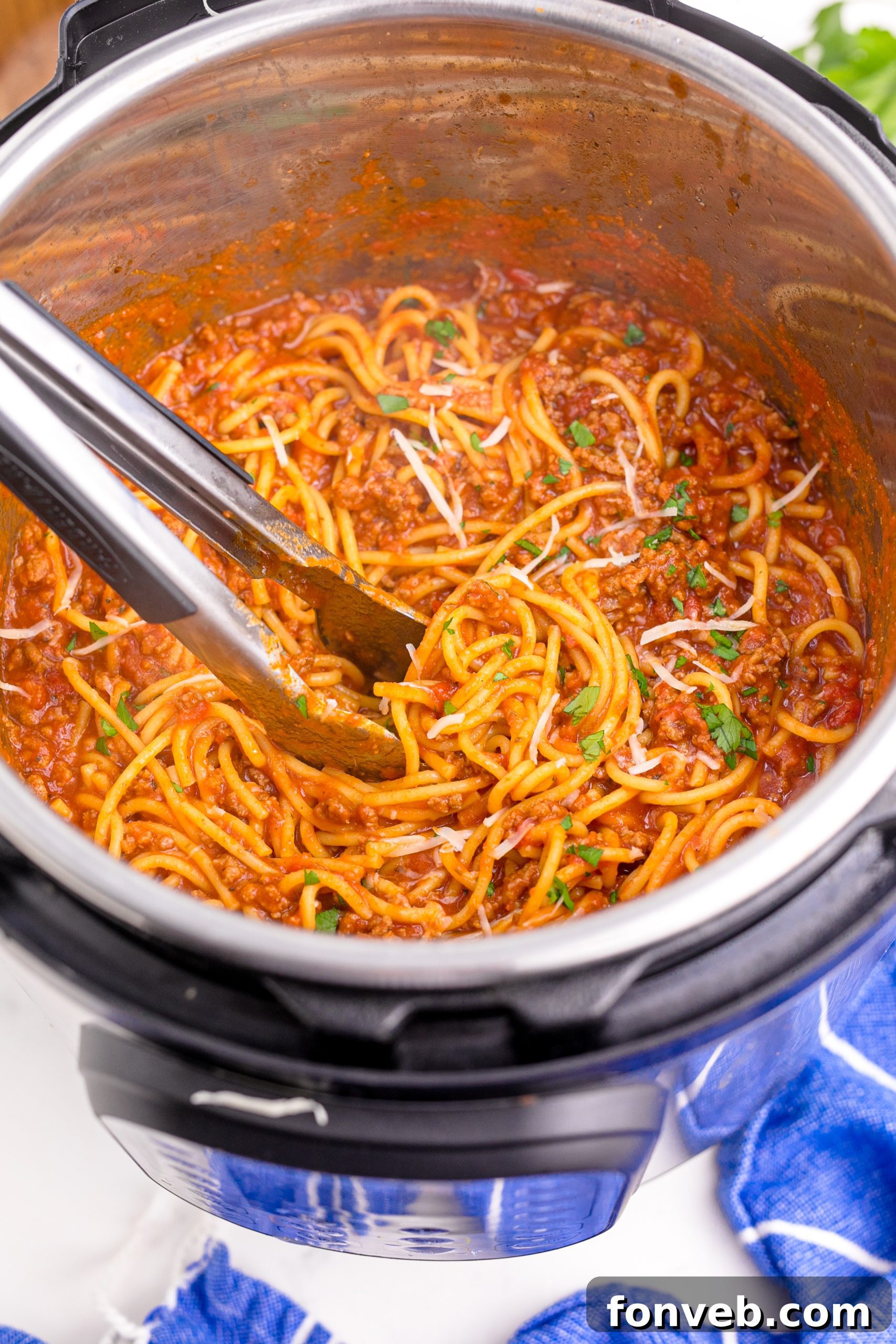 Instant Pot Spaghetti inthe instant pot being mixed with tongs sprinkled with parmesan cheese and parsley