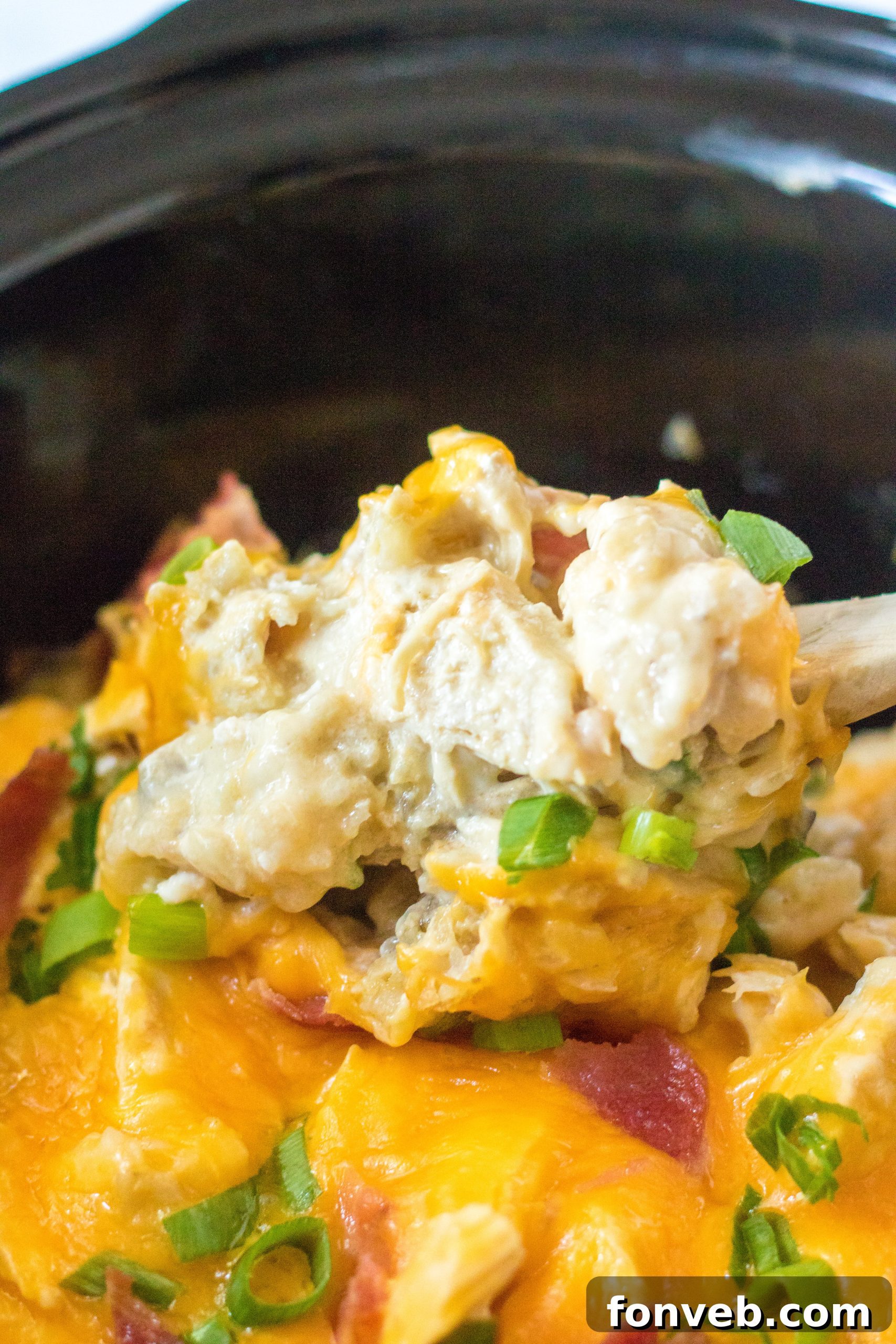slow cooker photo of a spoon lifting the chicken covered in cheese and tater tots, showing the delicious layers